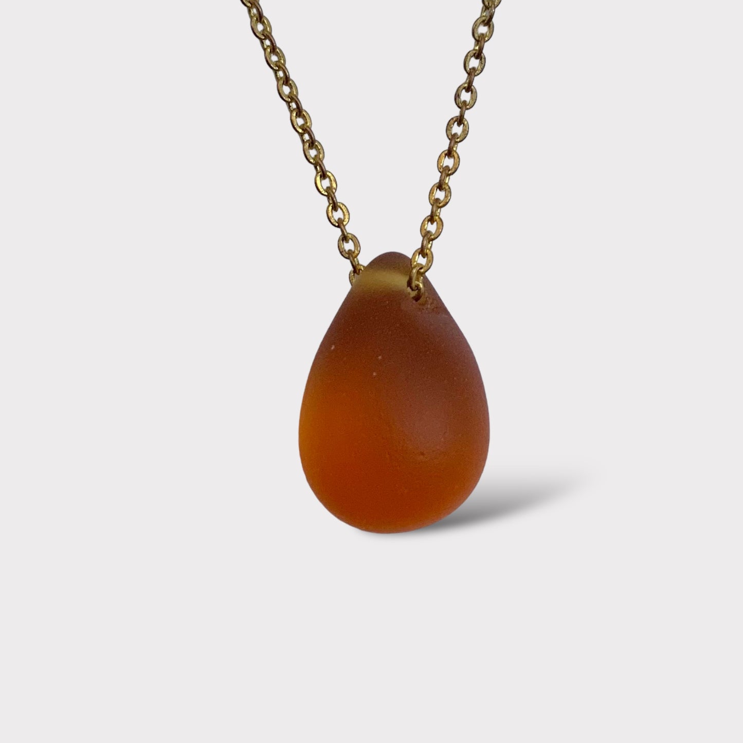 Amber matte teardrop pendant necklace with a smooth frosted finish, handcrafted and suspended on a delicate stainless steel chain. A warm and earthy accessory perfect for everyday wear or layering.