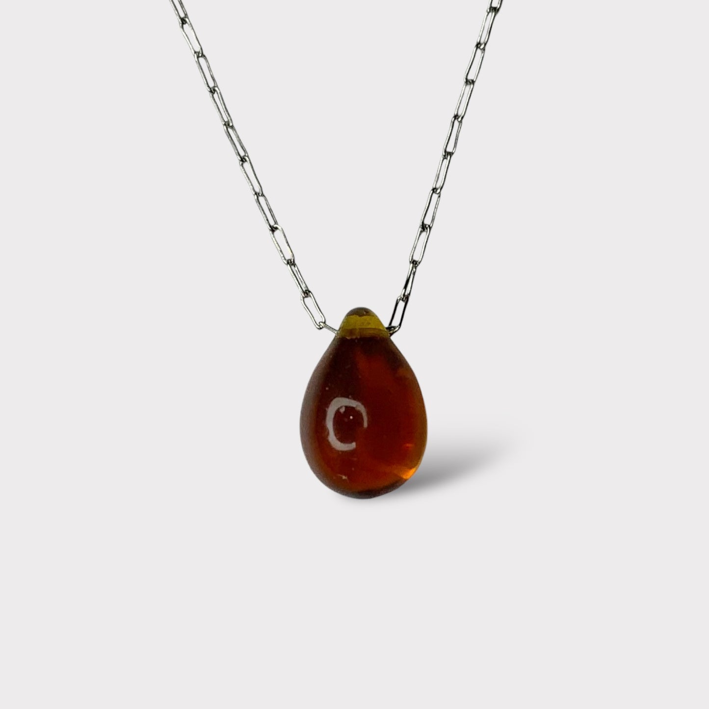 A warm amber translucent teardrop-shaped glass pendant, hanging from a stainless steel chain, displayed on a white background for a modern and artistic look.