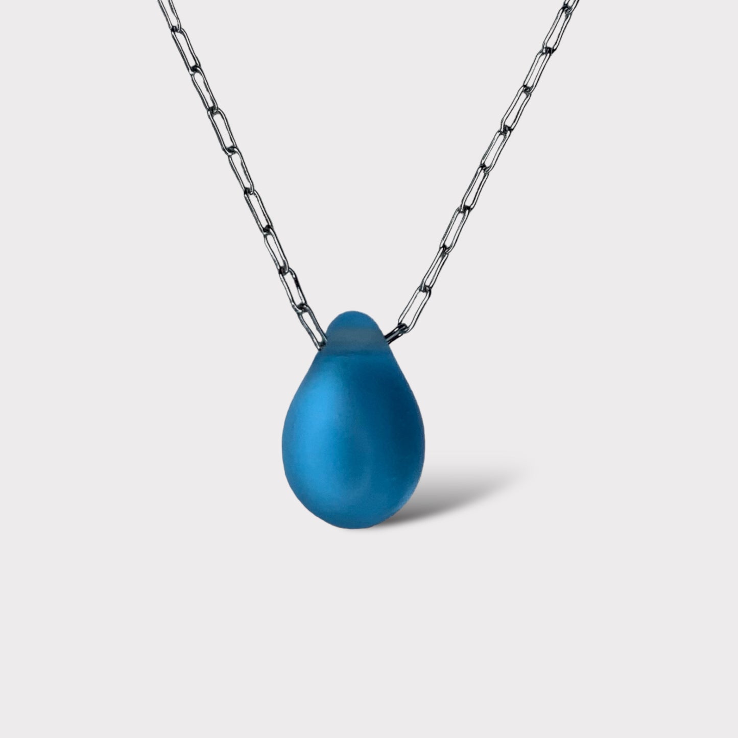 A vibrant aqua matte teardrop-shaped glass pendant, hanging from a stainless steel chain, styled on a clean white background for a fresh and modern look.