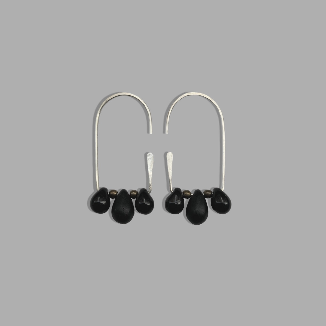A pair of handcrafted silver hoop earrings featuring three black teardrop glass pendants on each hoop, accented with brass beads. A sleek and modern accessory for a sophisticated look.