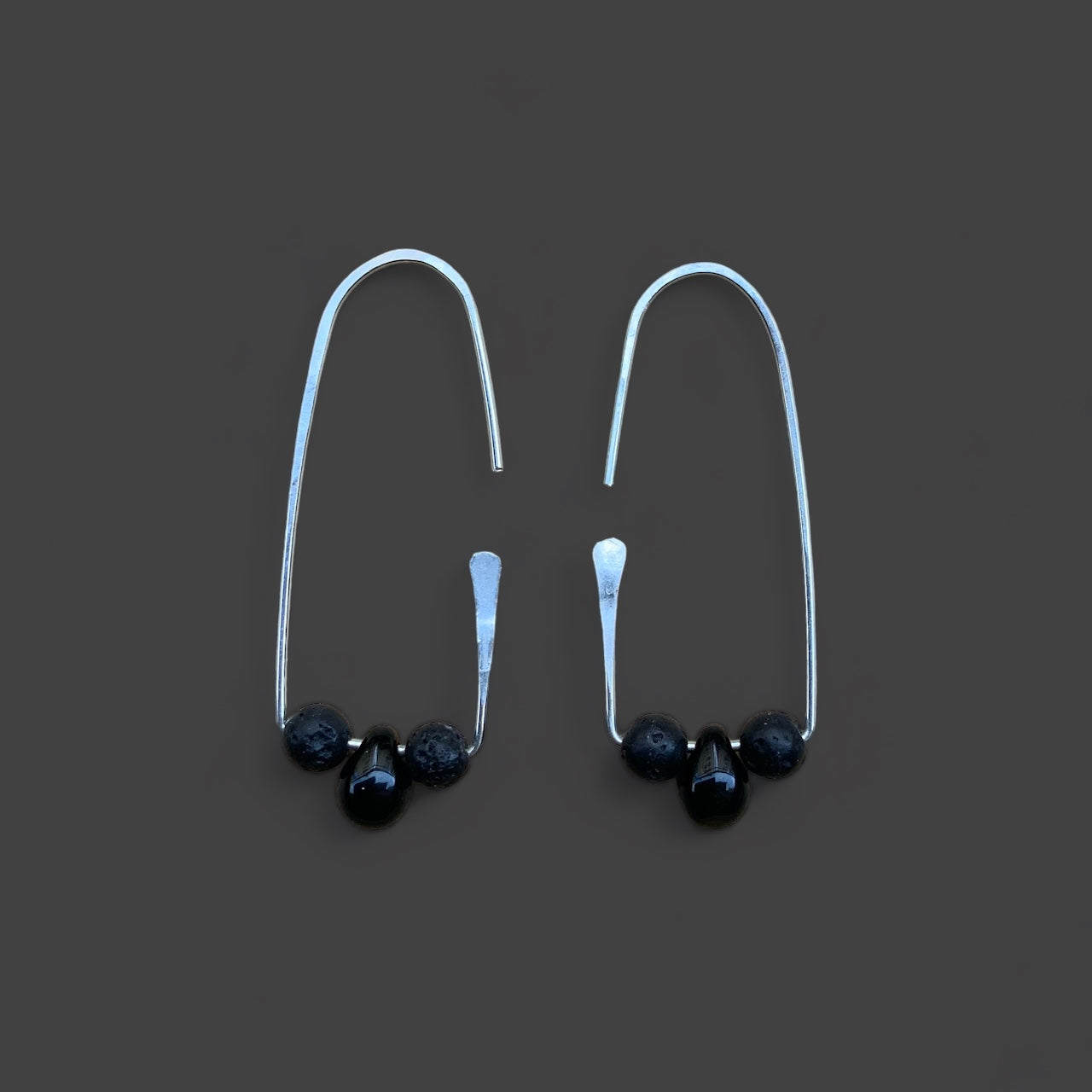 Silver handcrafted hoop earring with a smooth black glass and two lava stone beads, accented with a minimalist design. Displayed on a dark gray background for a sleek and modern look.
