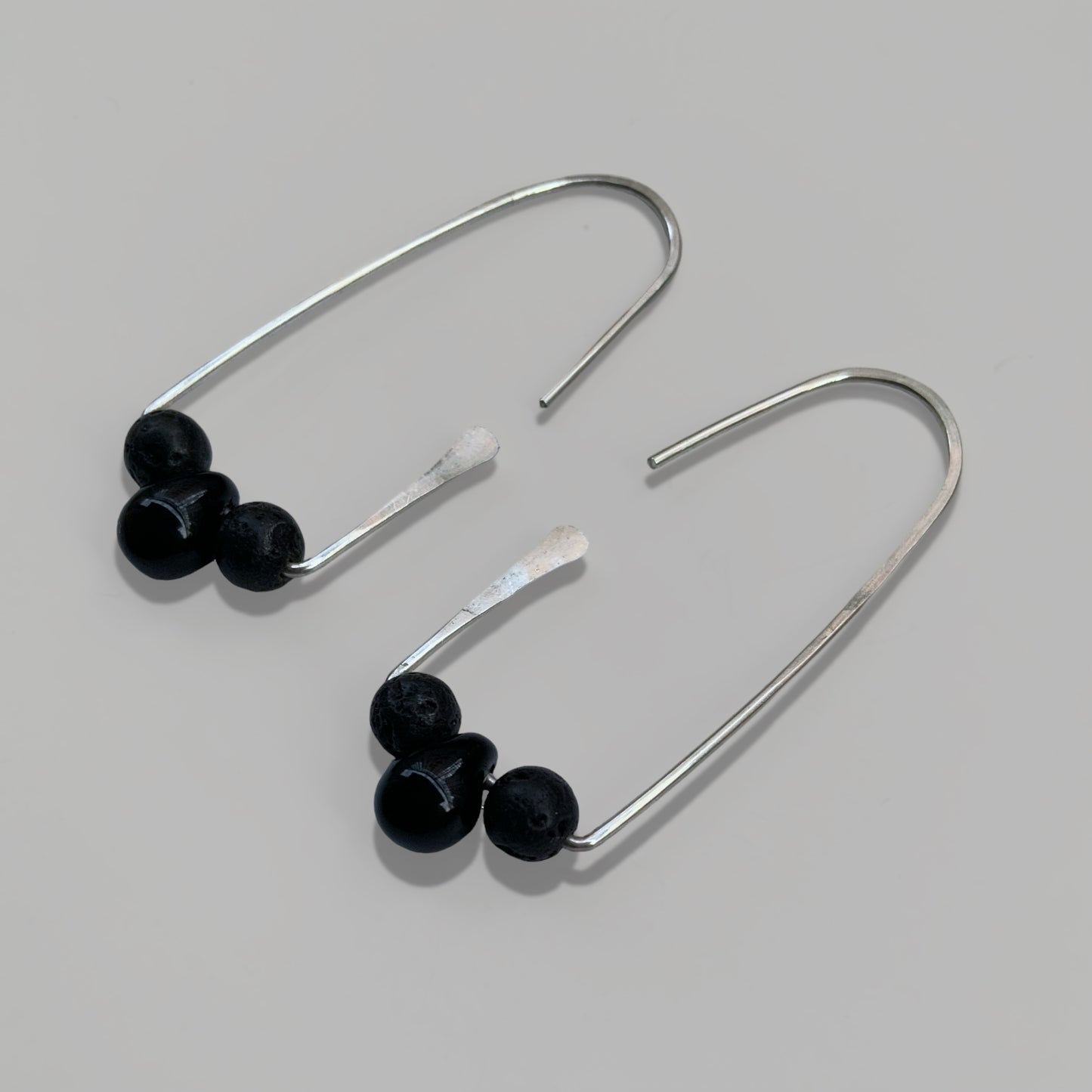 A pair of handcrafted silver hoop earrings featuring three black glass beads on each hoop, designed for a bold yet minimalist statement. Perfect for elevating any outfit.