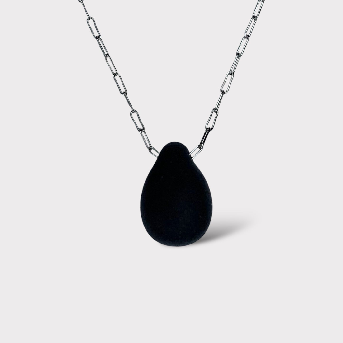A sleek black matte teardrop-shaped glass pendant, elegantly hanging from a stainless steel chain, styled on a white background for a bold and modern look.