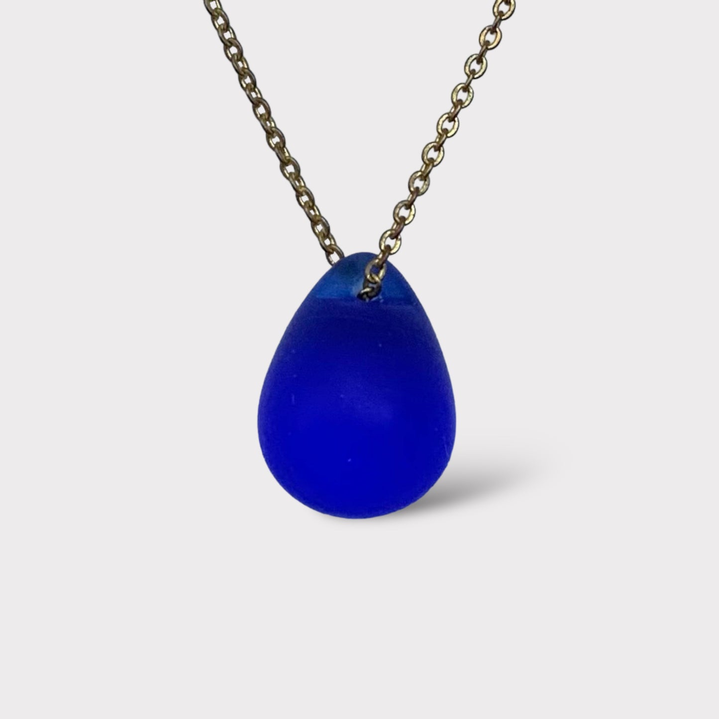 Cobalt blue matte teardrop glass pendant necklace featuring a frosted finish, hanging from a classic stainless steel chain. A bold and vibrant piece inspired by the deep Aegean Sea.