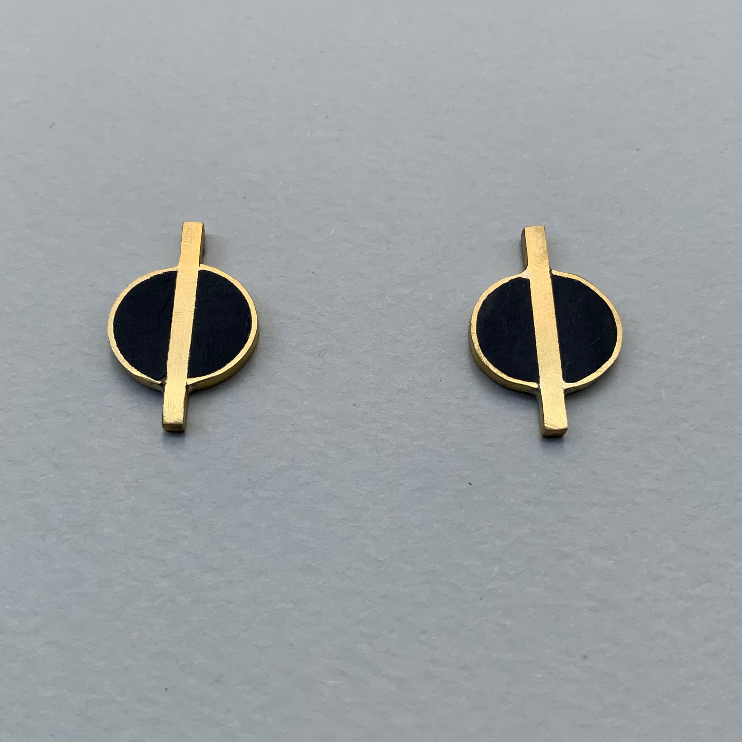 A close-up of geometric brass earrings featuring black circular accents and horizontal brass rods, styled against a dark background for a modern look