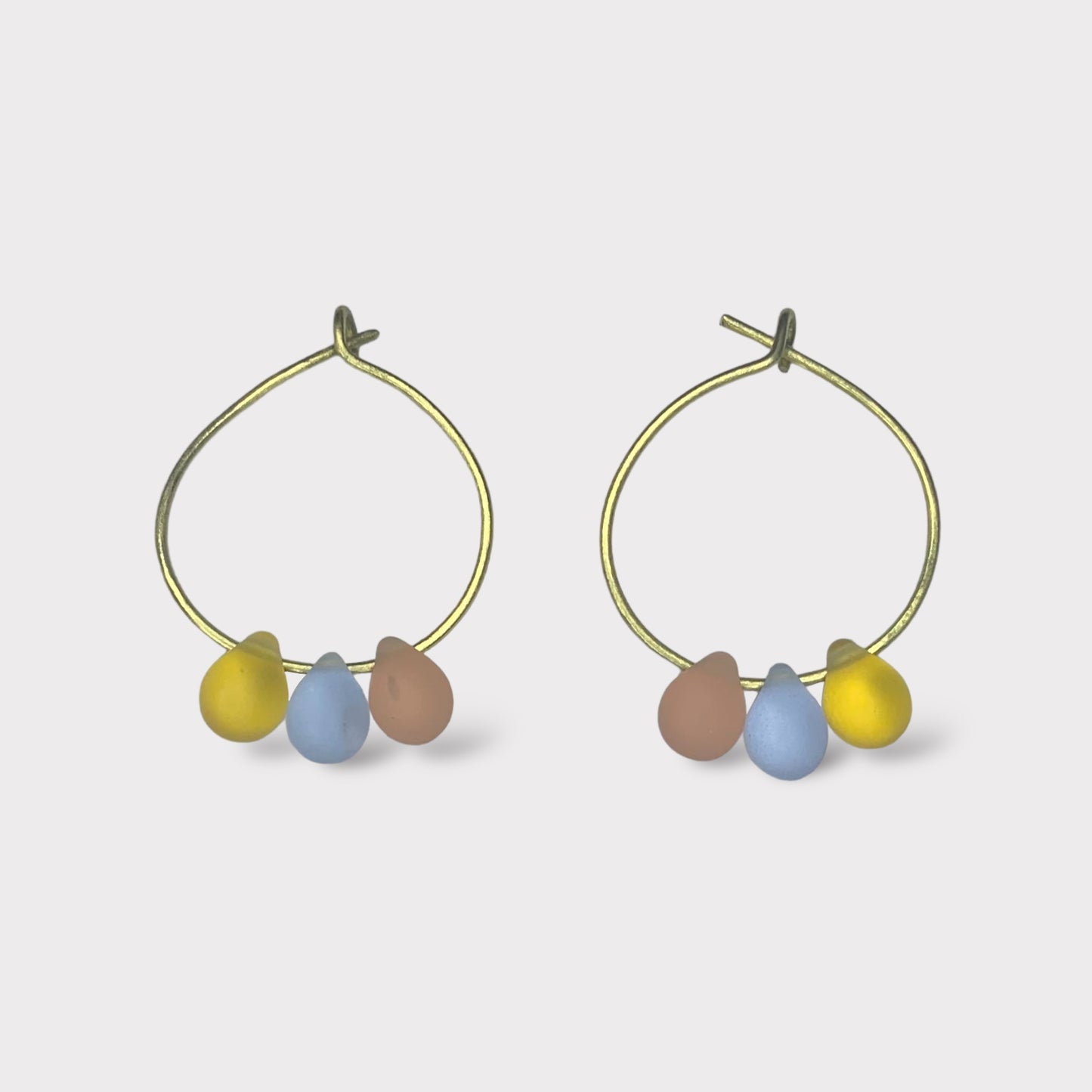 Playful gold hoop earrings featuring seaglass pendants in pastel pink, baby blue, and sunny yellow. A sweet and dreamy design reminiscent of cotton candy clouds.