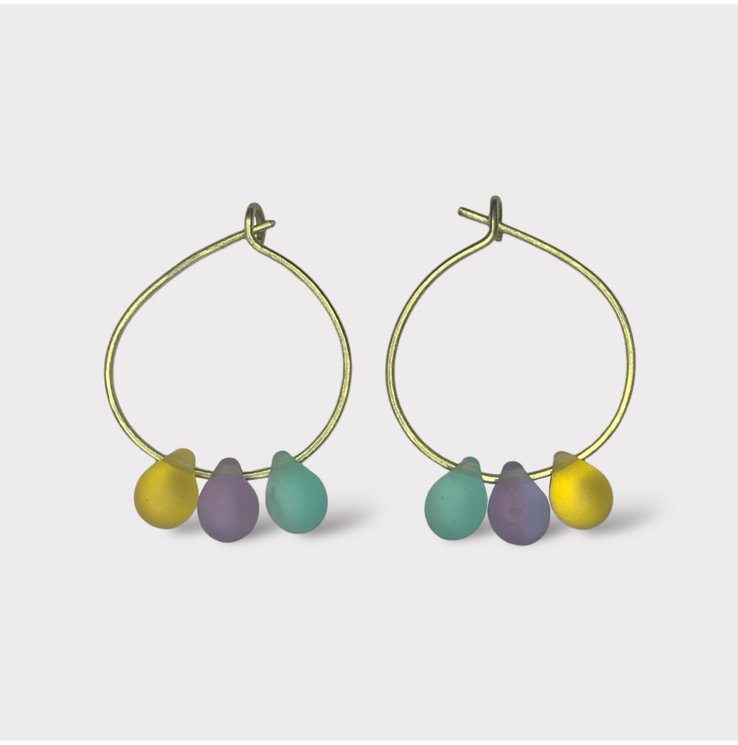 Playful gold hoop earrings featuring seaglass pendants in pastel pink, baby blue, and sunny yellow. A sweet and dreamy design reminiscent of cotton candy clouds.