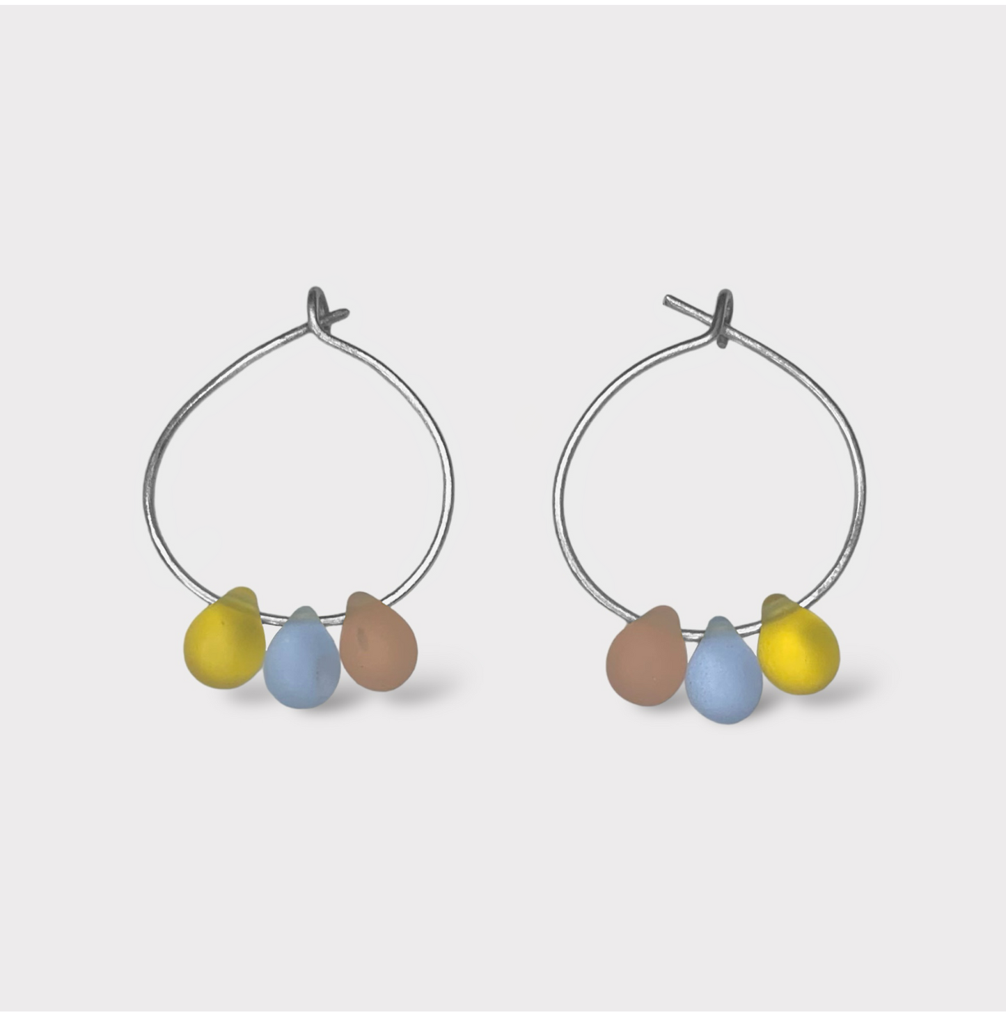 Playful silver hoop earrings featuring seaglass pendants in pastel pink, baby blue, and sunny yellow. A sweet and dreamy design reminiscent of cotton candy clouds.