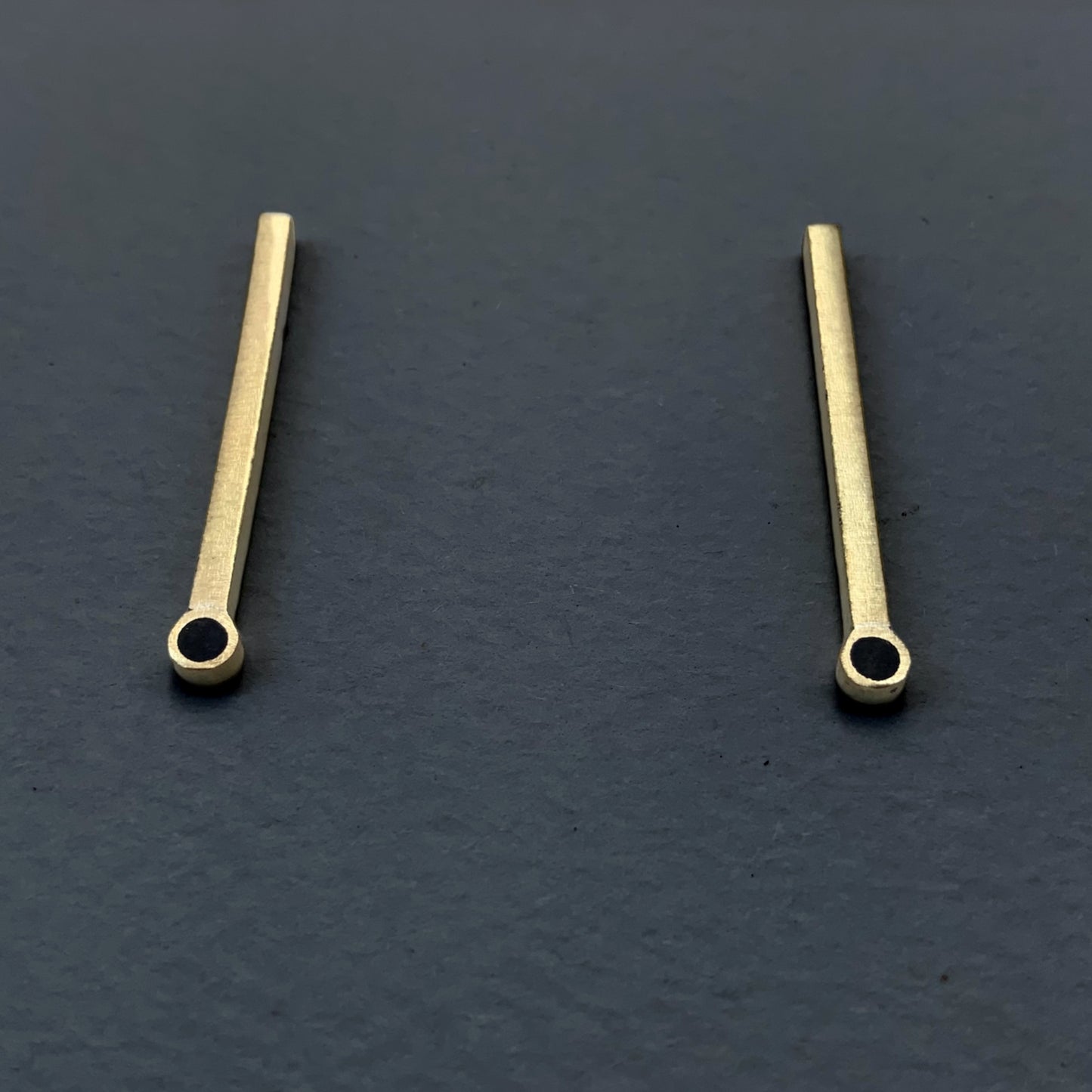 Handcrafted brass bar earrings featuring a circular cutout at the bottom, styled on a dark gray background for a bold contrast