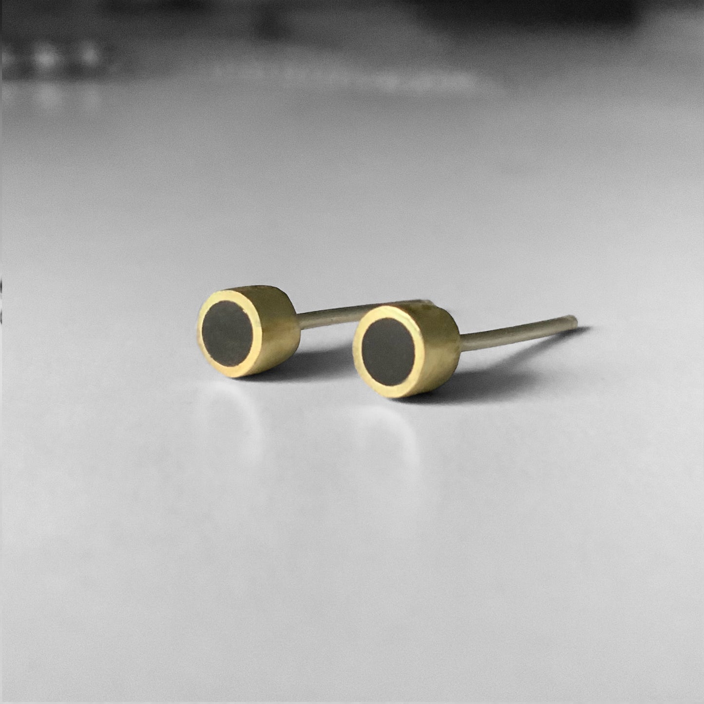 A close-up of brass stud earrings featuring black circular accents, styled on a light background to highlight their modern geometric design