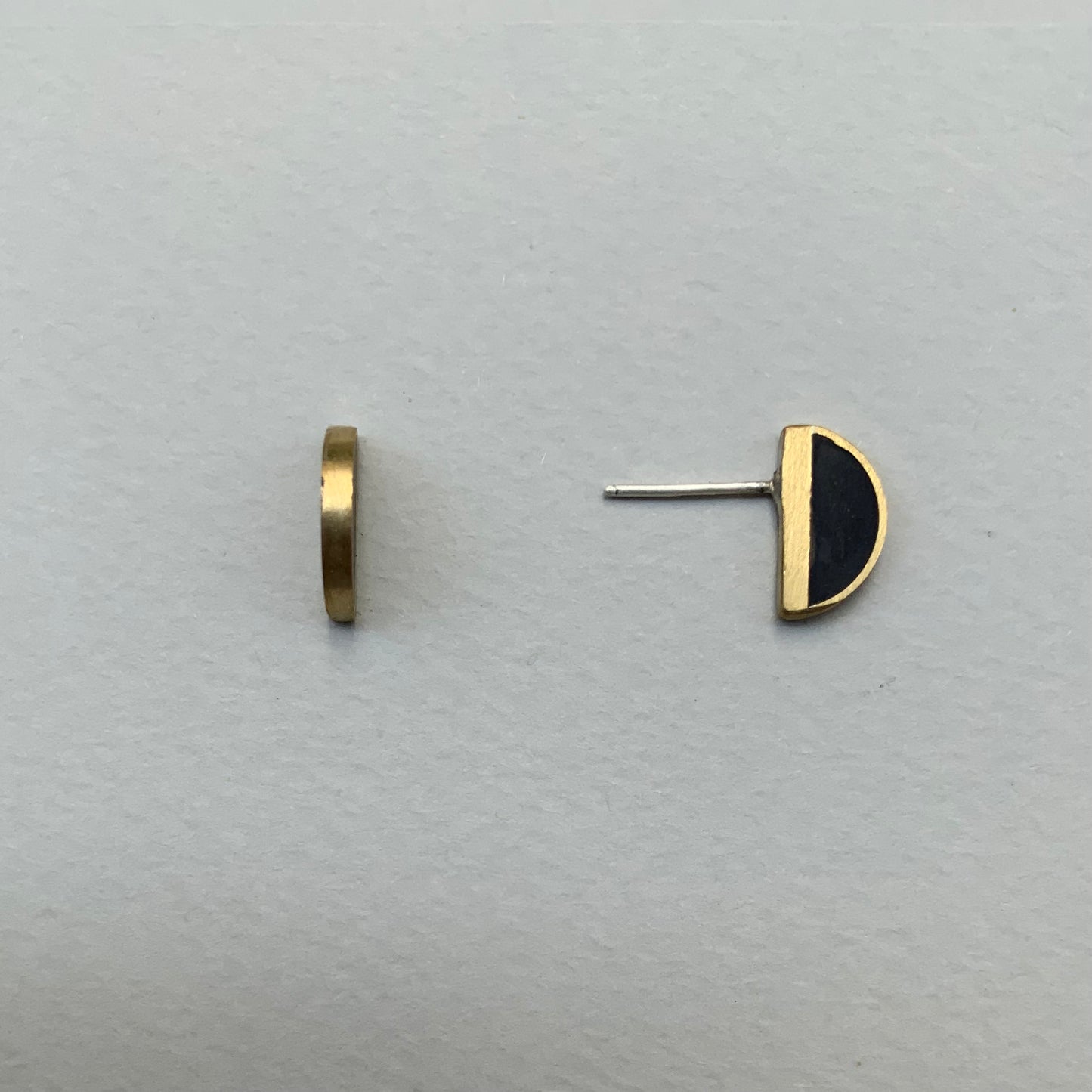 Close-up of brass half-cirlce earrings featuring black inlays, with one earring showing a side view and the other a front view, arranged on a light gray surface