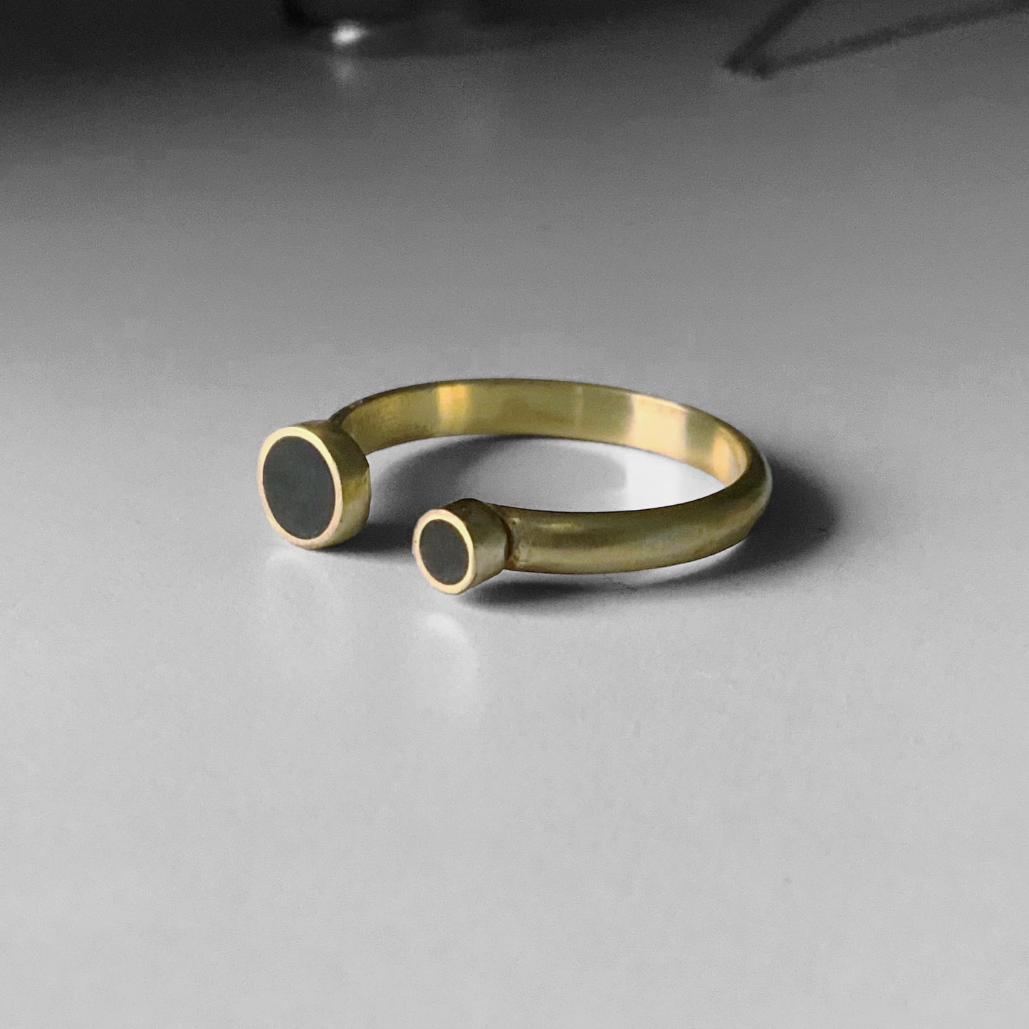 A handcrafted open gold ring featuring two black circular inlays of different sizes, styled on a light gray background to showcase its minimalist and modern design.