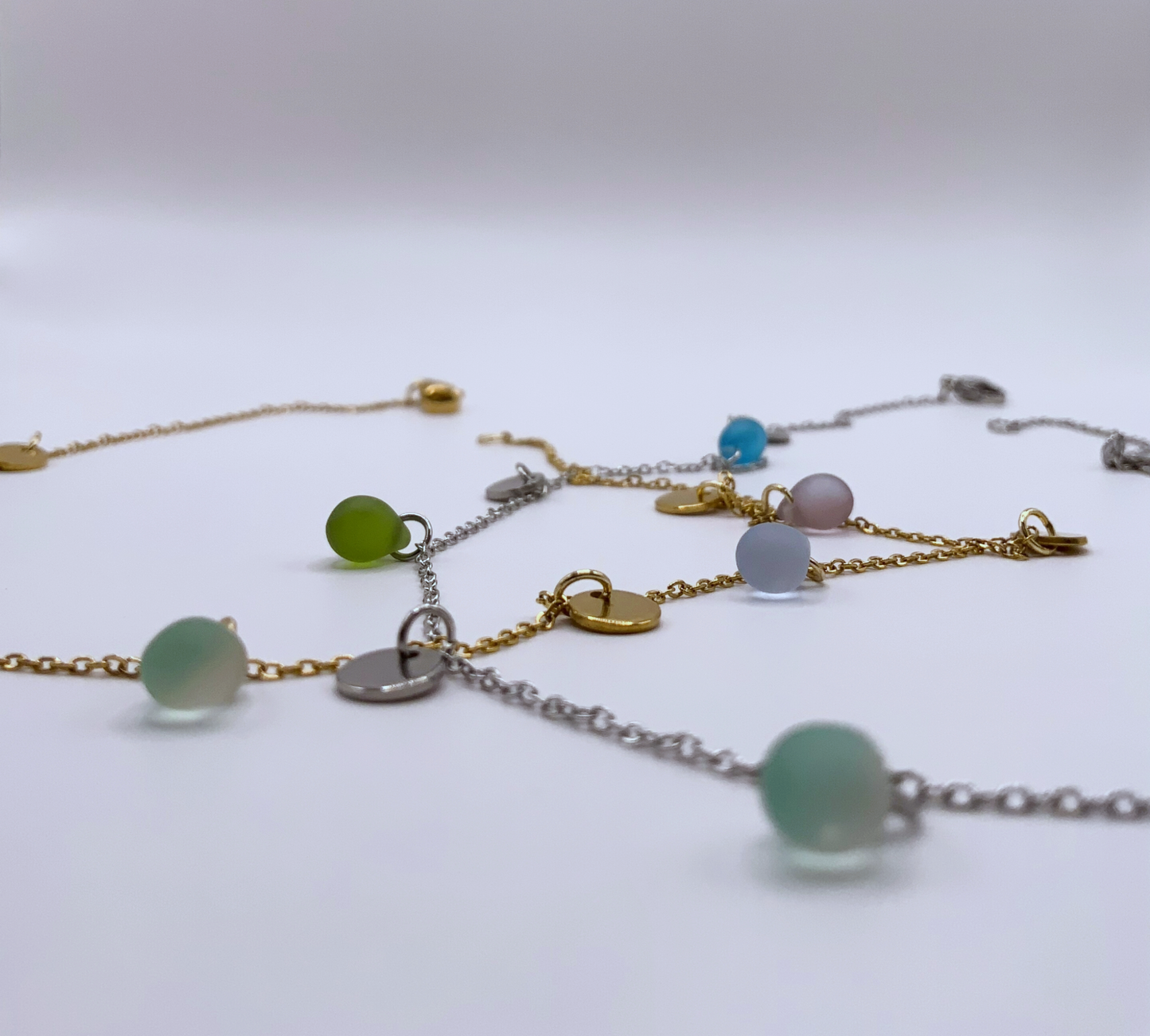 Silver and gold chain necklaces with pastel frosted glass beads and coin charms, handcrafted in Greece. A modern, minimalist design perfect for layering or gifting.