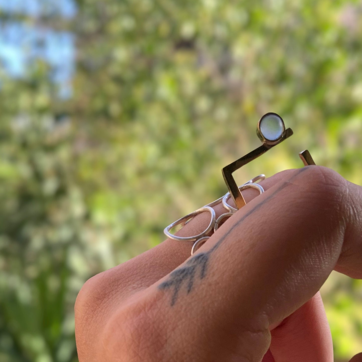 Artisan gold ring with a minimalist circular accent in a frosted glass design, displayed on a hand against a natural outdoor background.