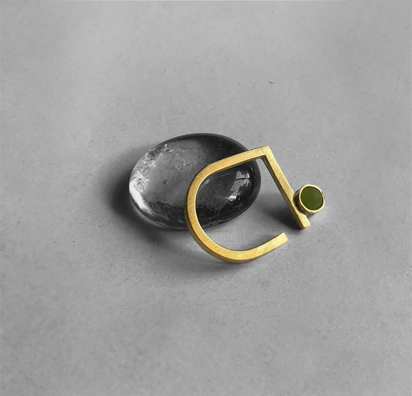 Minimalist gold ring featuring a frosted olive green glass accent, displayed on a transparent pebble for a contemporary style.