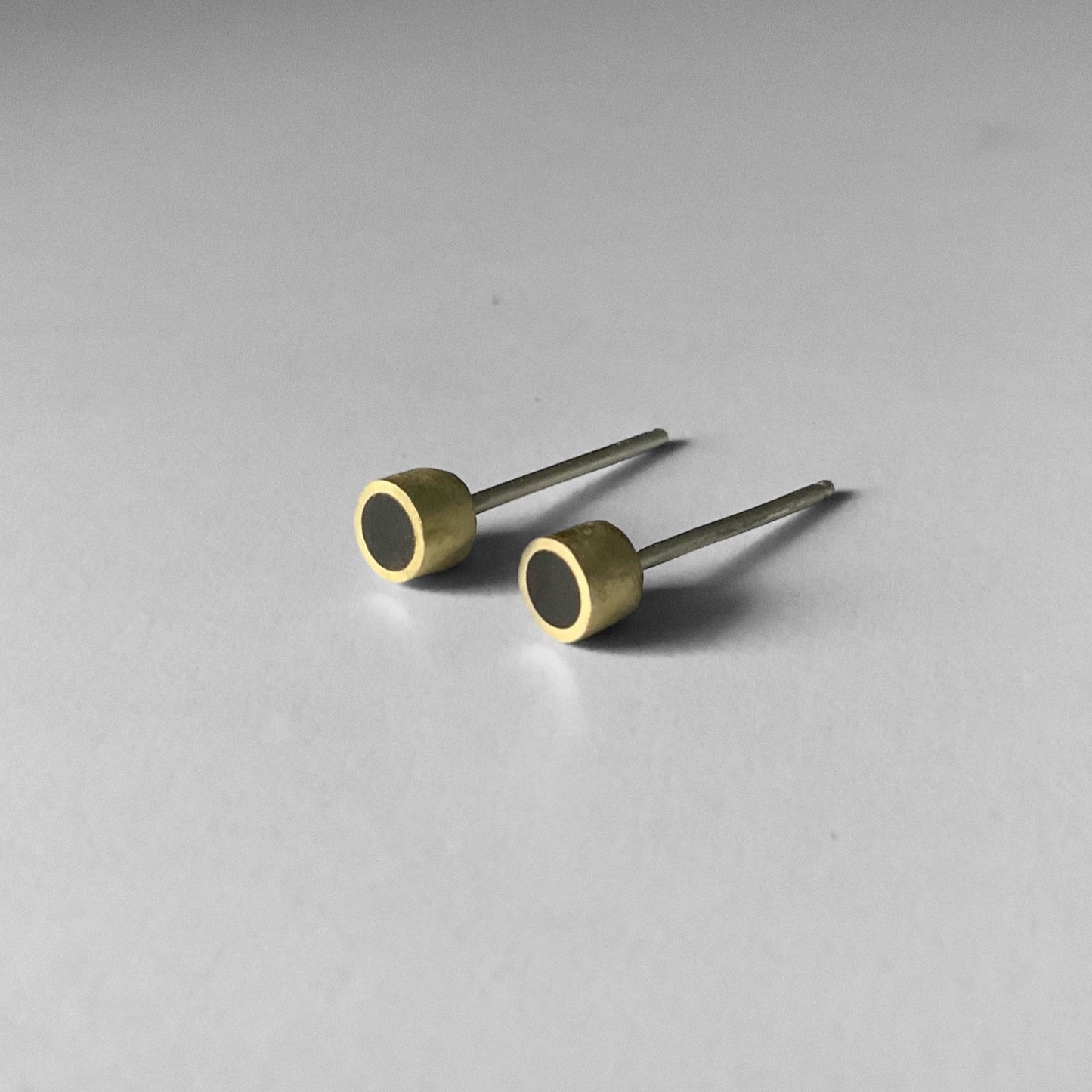 A pair of handcrafted brass stud earrings with a black circular inlay, displayed on a light gray surface to emphasize their sleek and minimalist design
