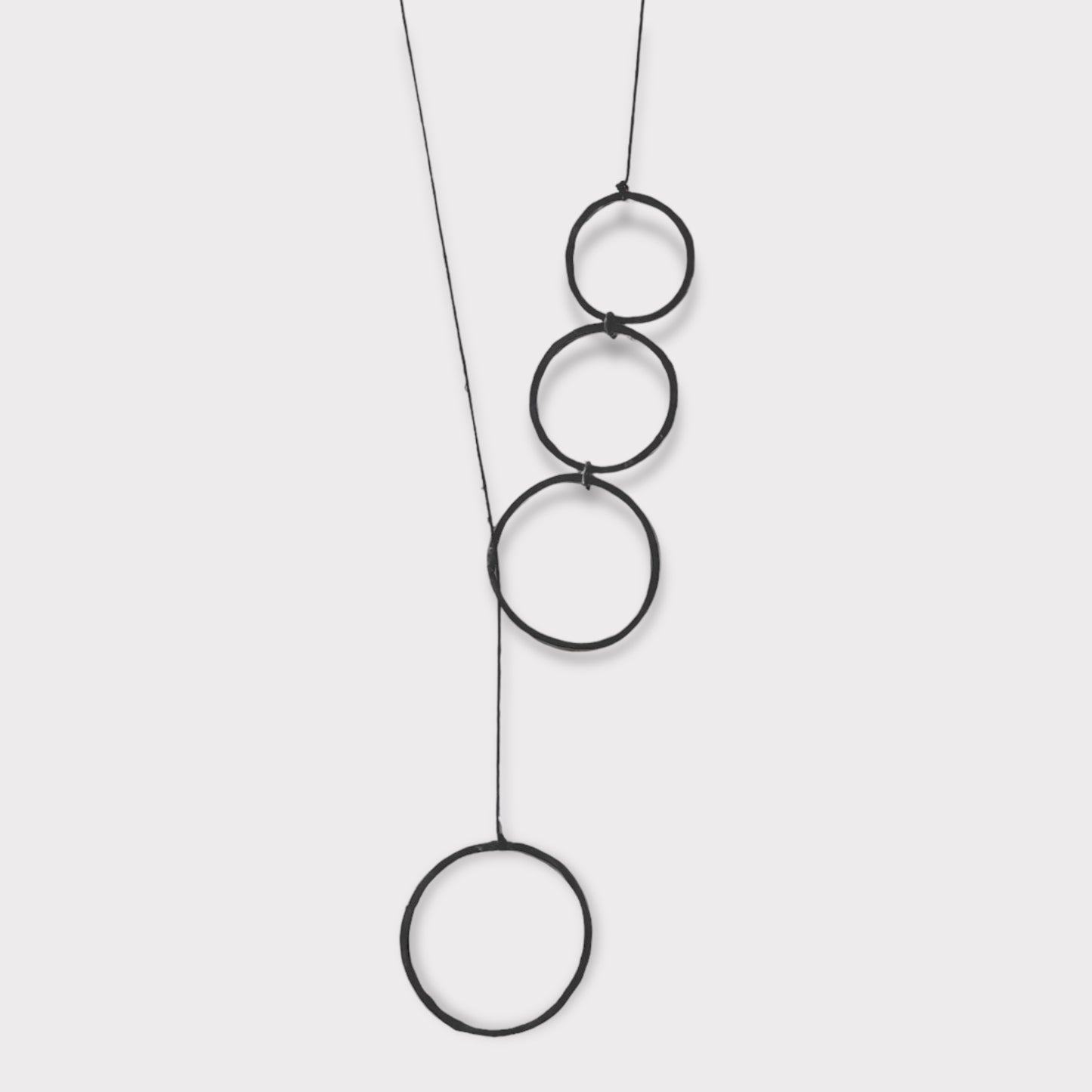 A handcrafted necklace featuring cascading open brass circles linked together, suspended on a minimalist cord, displayed on a clean white background to highlight its geometric simplicity.