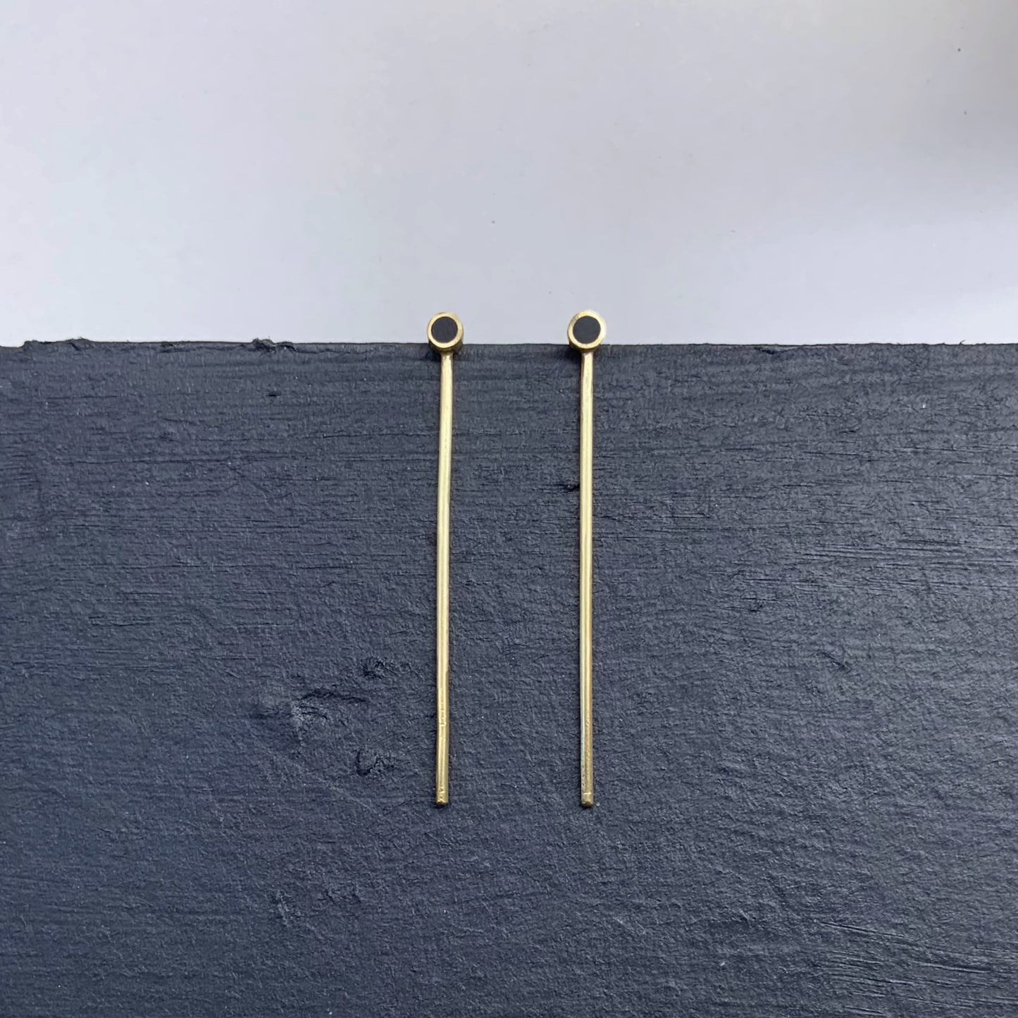 Handmade gold earrings featuring a long minimalist bar with black circular accents, designed for contemporary styles