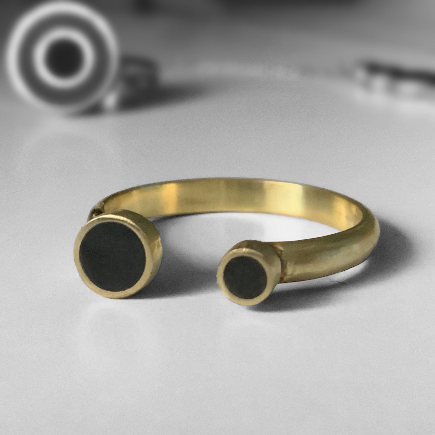 A close-up of an open gold ring with two black circular accents, one larger and one smaller, displayed on a light gray surface for a sleek and modern look