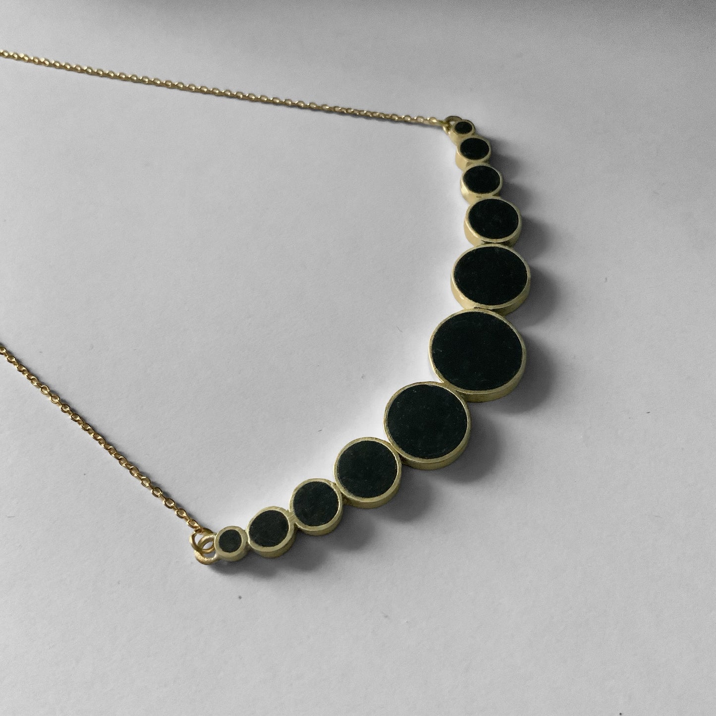 A handcrafted brass necklace with black circular accents, designed in a gradient style, photographed close-up to highlight the intricate details of the piece.