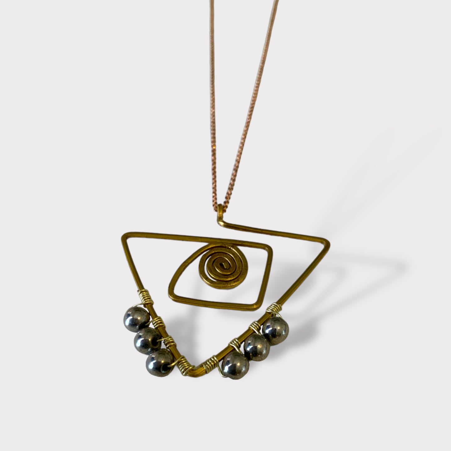 A minimalist brass necklace with an abstract triangle frame, spiral detail, and metallic bead accents, styled on a white background to highlight its unique and artistic design