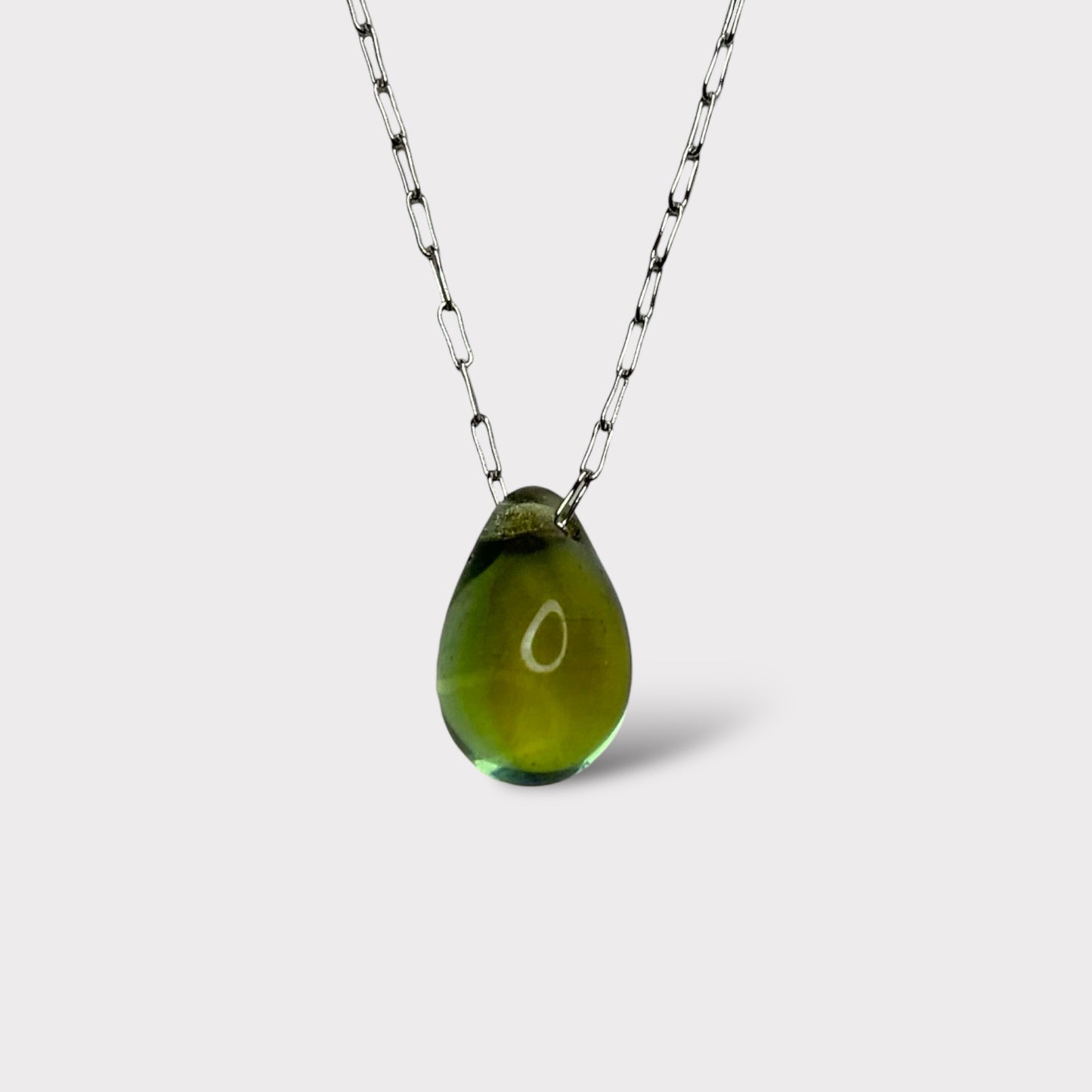 A minimalist necklace featuring an iridescent teardrop-shaped glass pendant, elegantly suspended on a stainless steel chain, styled on a white background.