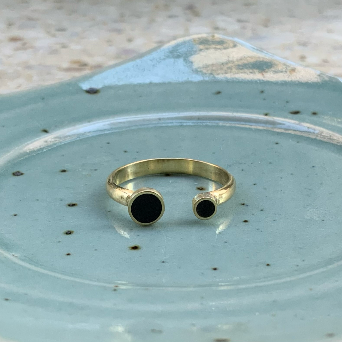 A handcrafted open gold artisan ring with black circular inlays, elegantly displayed on a speckled ceramic plate for an artistic and rustic presentation