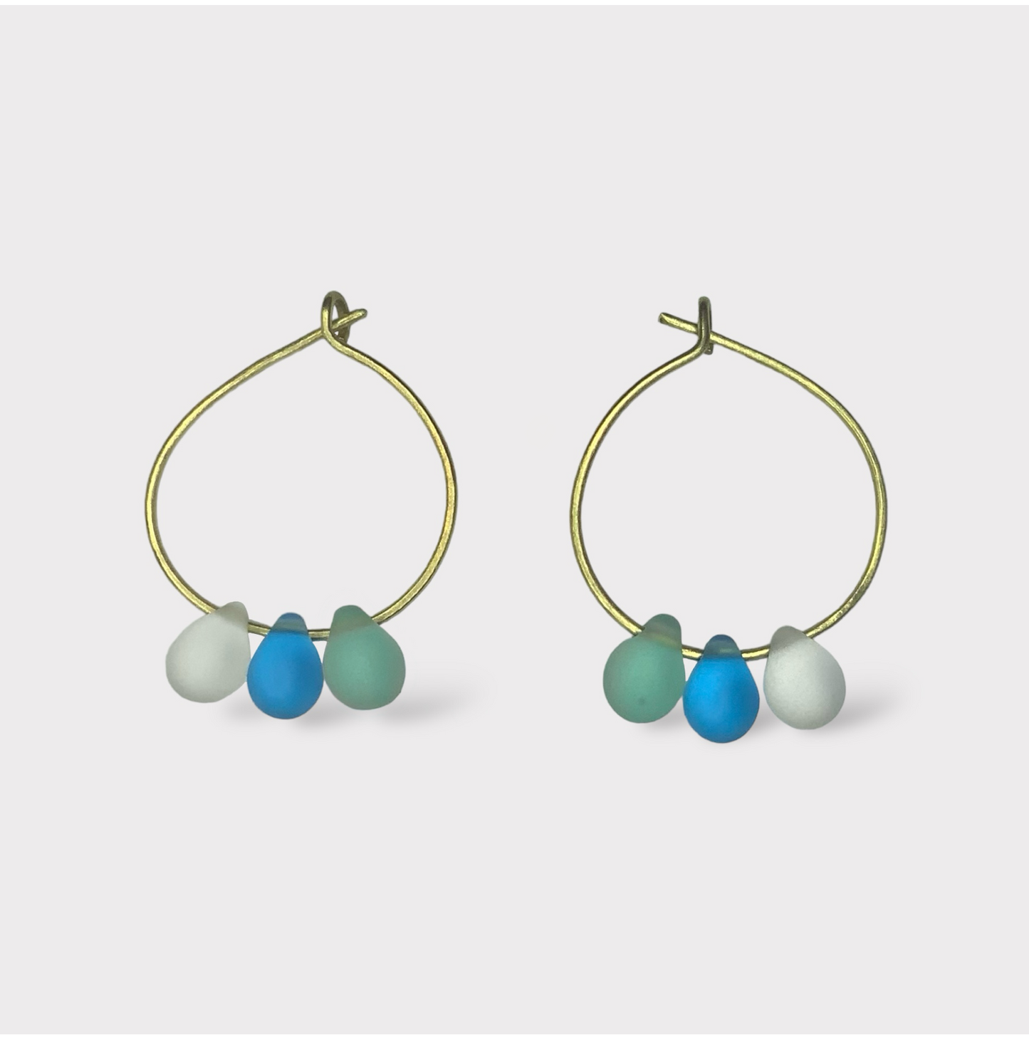 Playful gold hoop earrings adorned with aqua, turquoise, and seafoam green seaglass charms. A breezy and refreshing design reminiscent of seaside popsicles.
