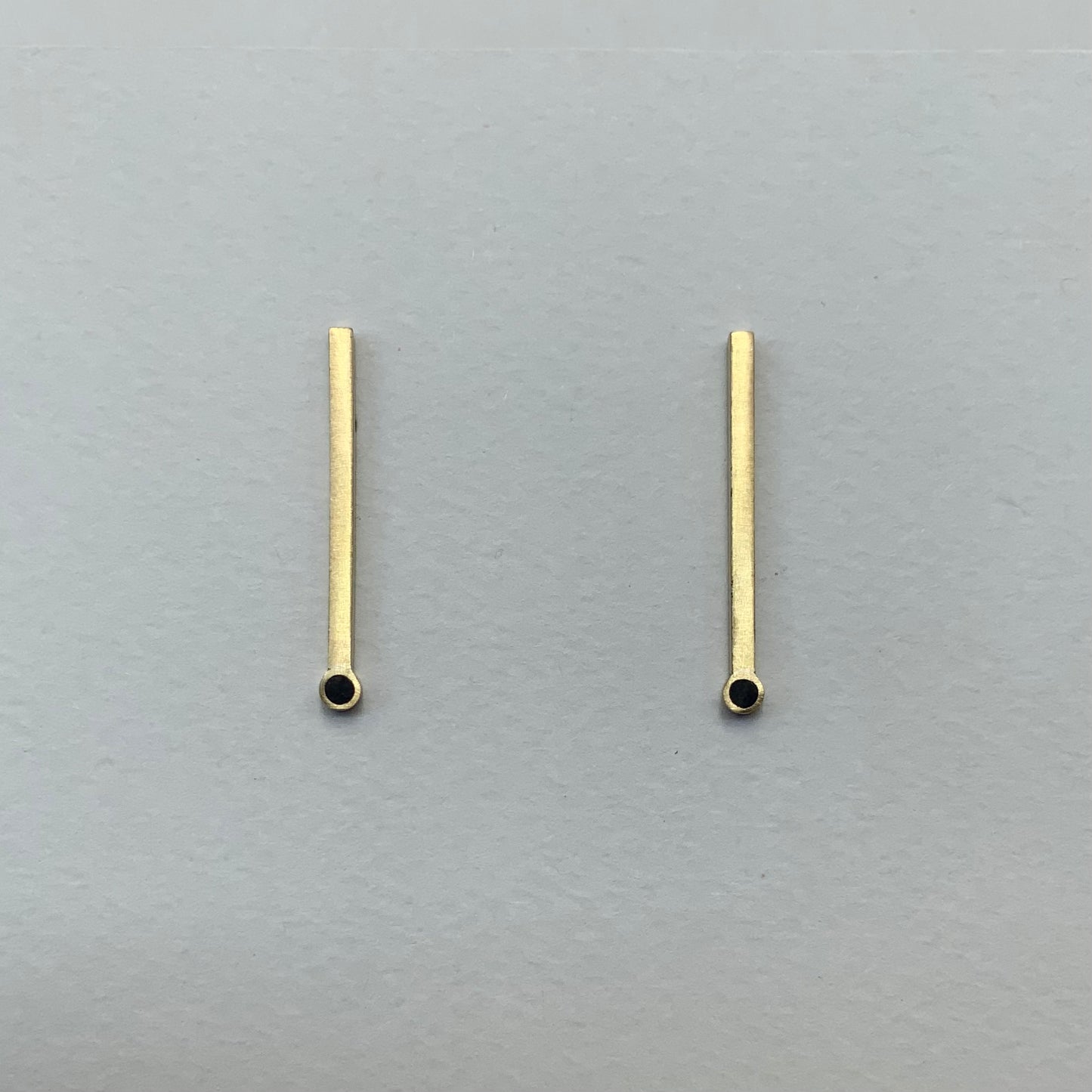 Minimalist brass bar earrings with a circular cutout detail, displayed on a light gray background to emphasize their modern and geometric aesthetic