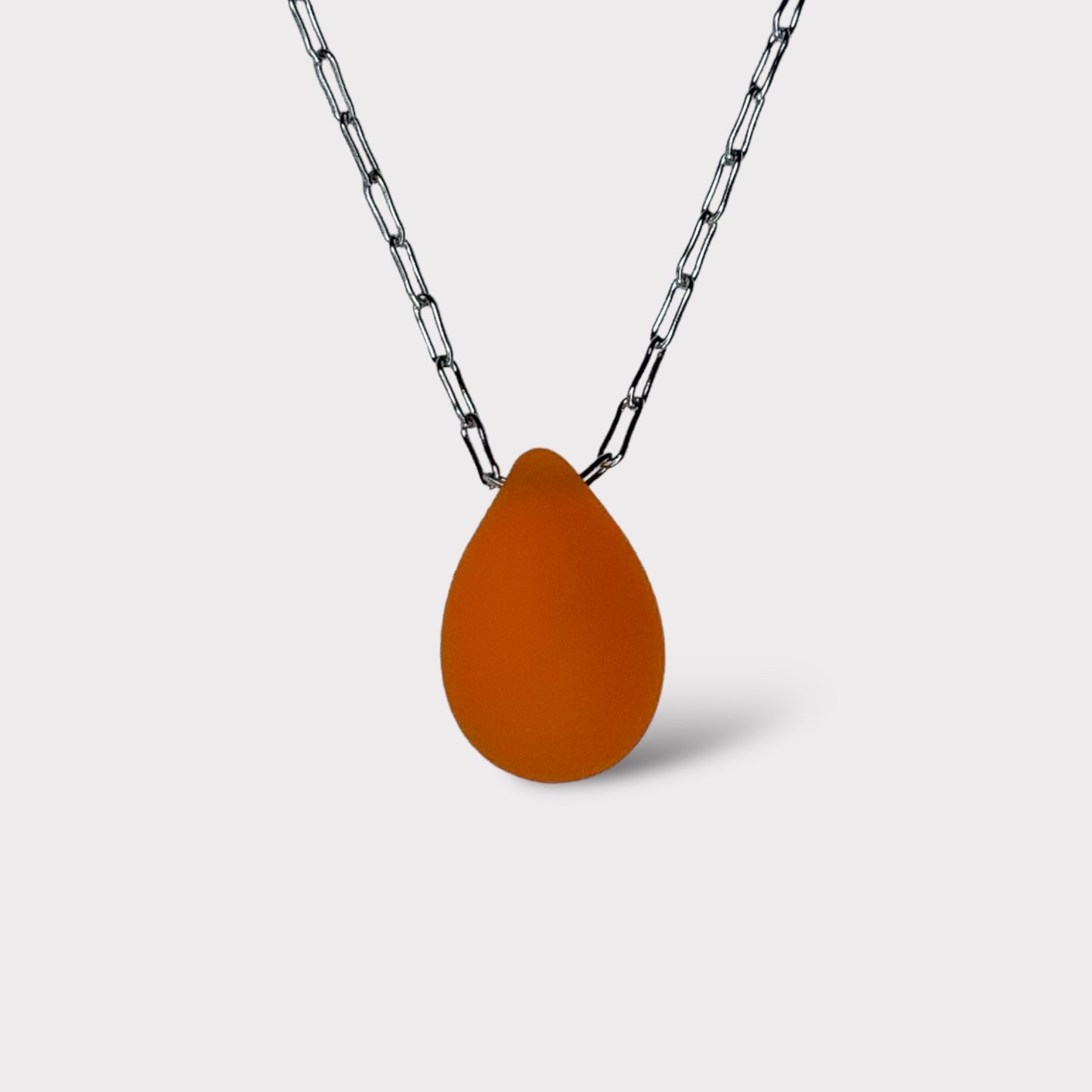 A vibrant tangerine matte teardrop-shaped glass pendant, hanging from a stainless steel chain, displayed on a white background for a striking and modern design.