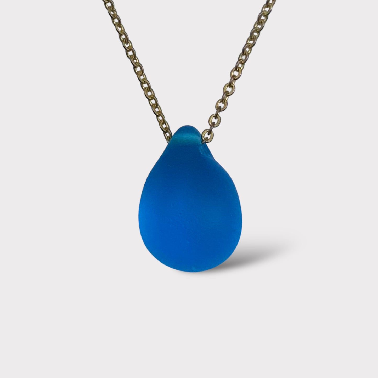 Turquoise matte teardrop glass pendant necklace featuring a frosted finish, hanging from a classic stainless steel chain. A bold and vibrant piece inspired by the Mediterranean sea horizon