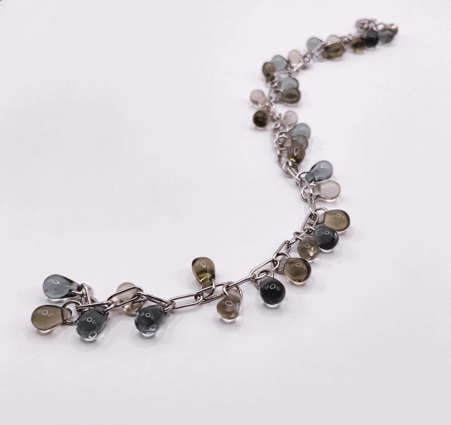 Curved silver chain bracelet featuring shiny glass teardrop charms, arranged on a clean white surface