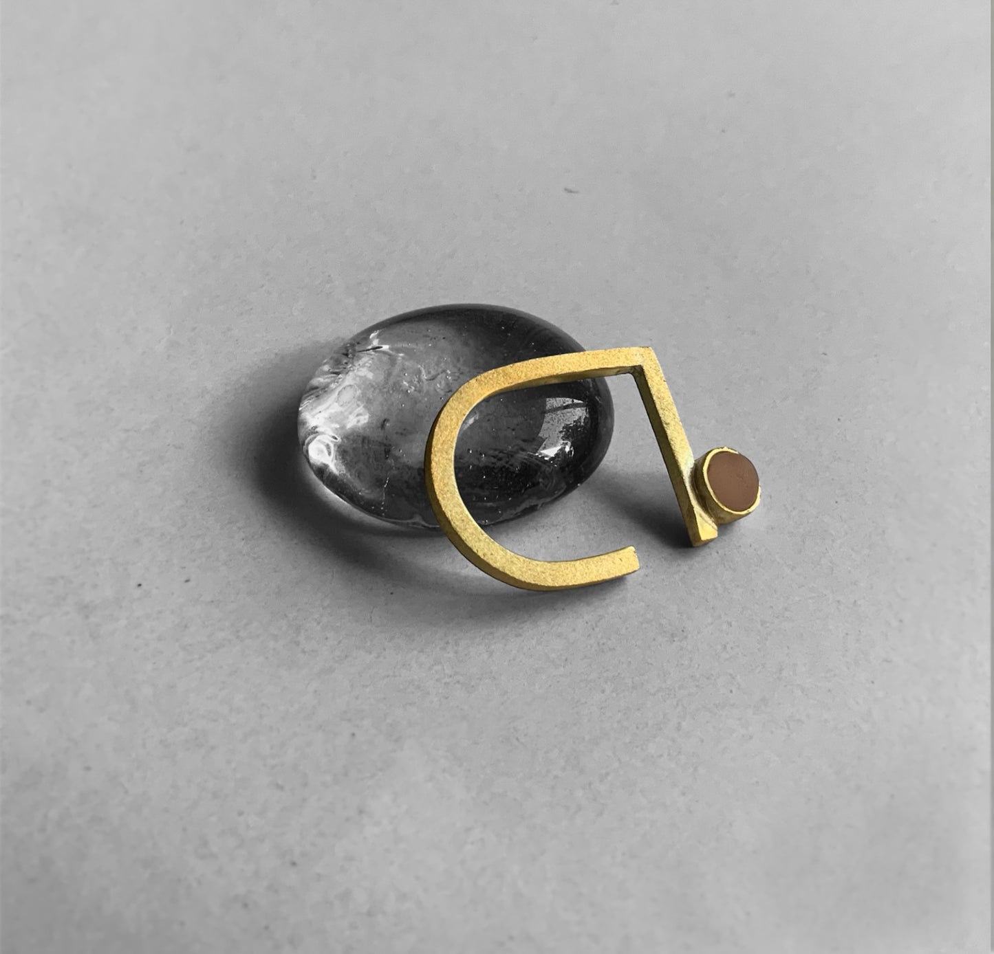 Gold ring with a frosted peach glass accent, displayed on a glass pebble on a gray background.