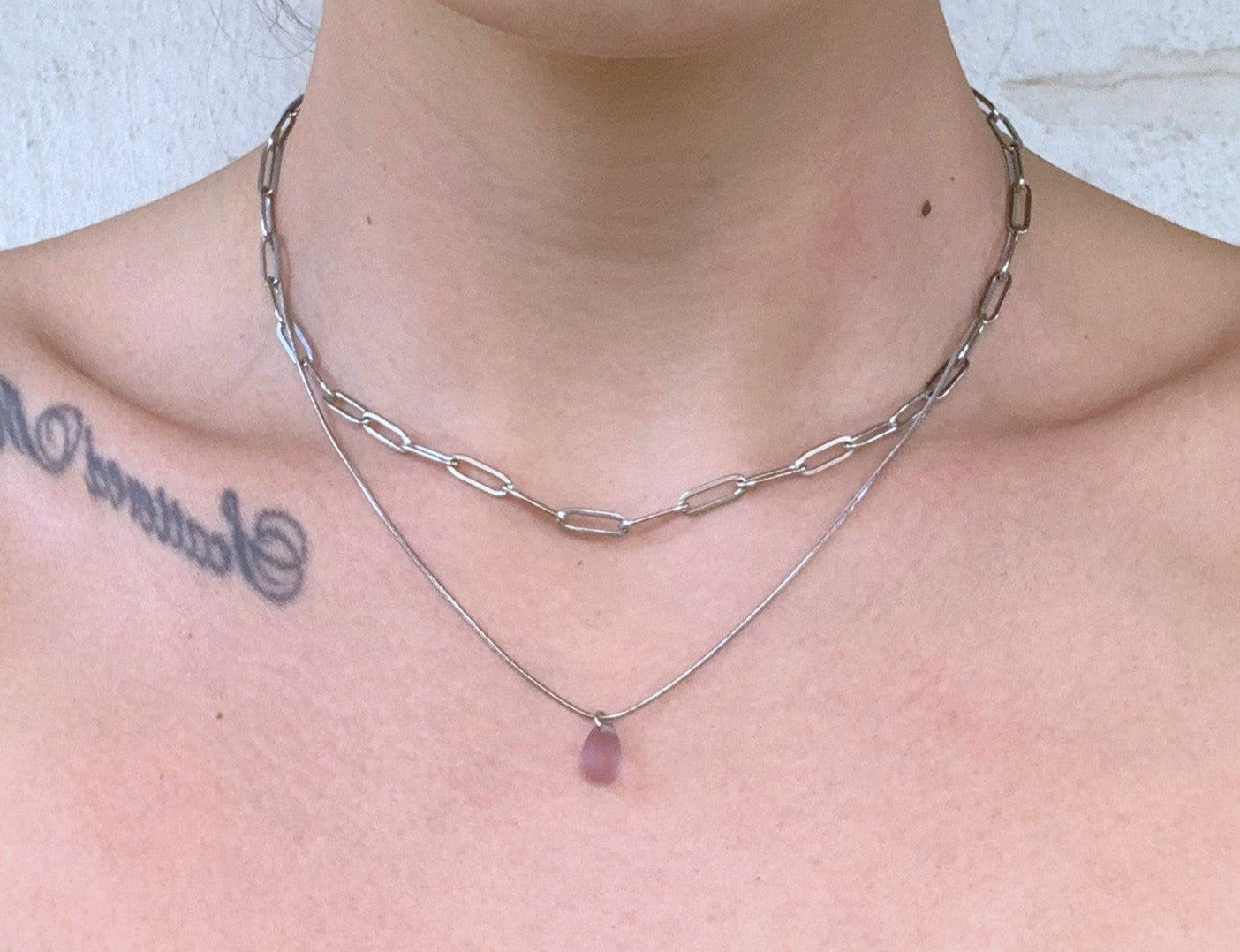 Layered silver chain necklace with a lavender frosted glass teardrop pendant, featuring a chunky cable chain and a sleek snake chain. Shown on a model's neckline.