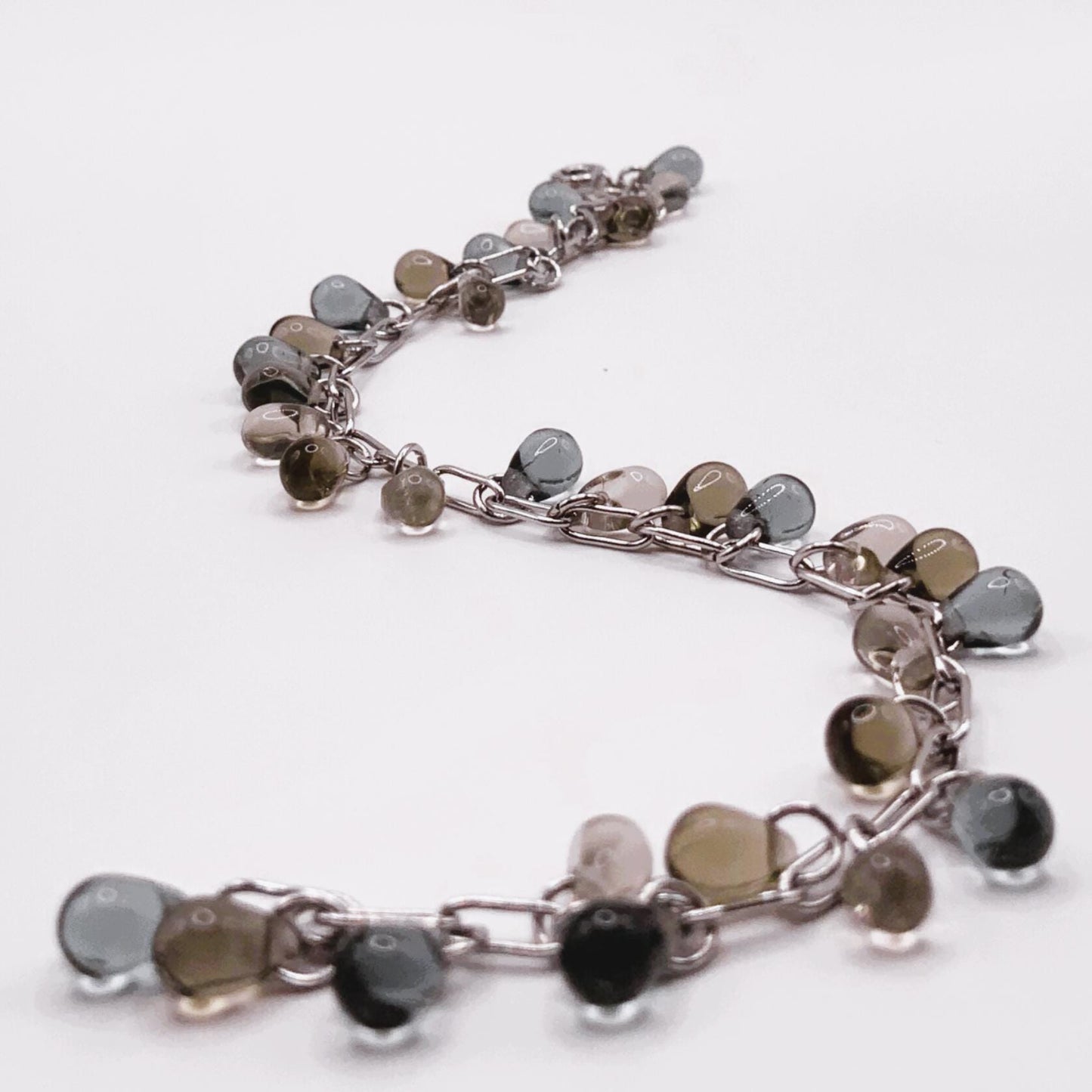 Chunky silver chain bracelet with glass teardrop charms in earthy tones displayed in a curved layout on a white background.