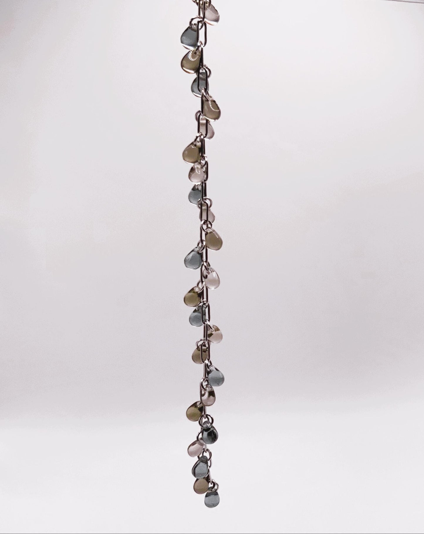 Silver chain bracelet with shiny glass teardrop charms in earthy tones, displayed vertically against a white background