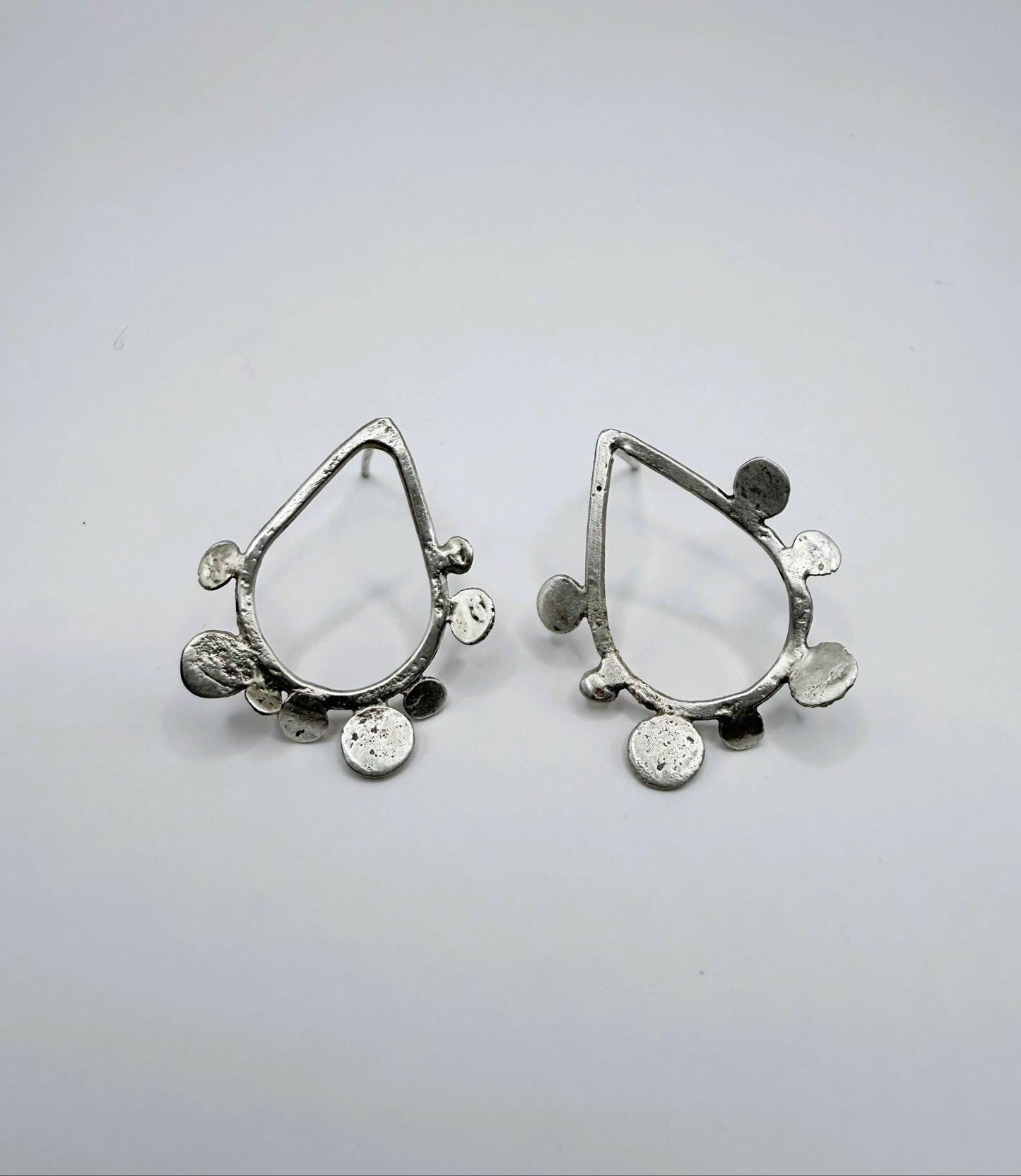 Front view of sterling silver teardrop stud earrings with textured dot disc details on a white background