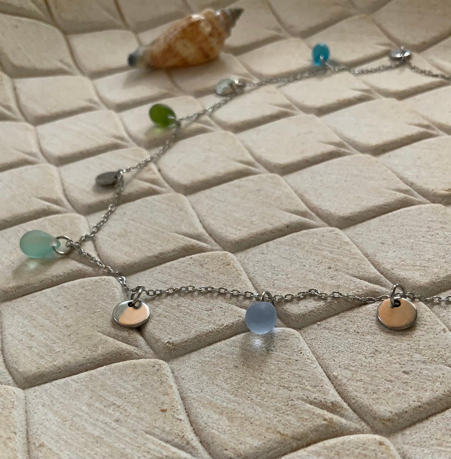 Delicate silver necklace with small sea glass beads and silver coin pendants, displayed on white stone tiles, handmade in Greece by Jewelry by Meow