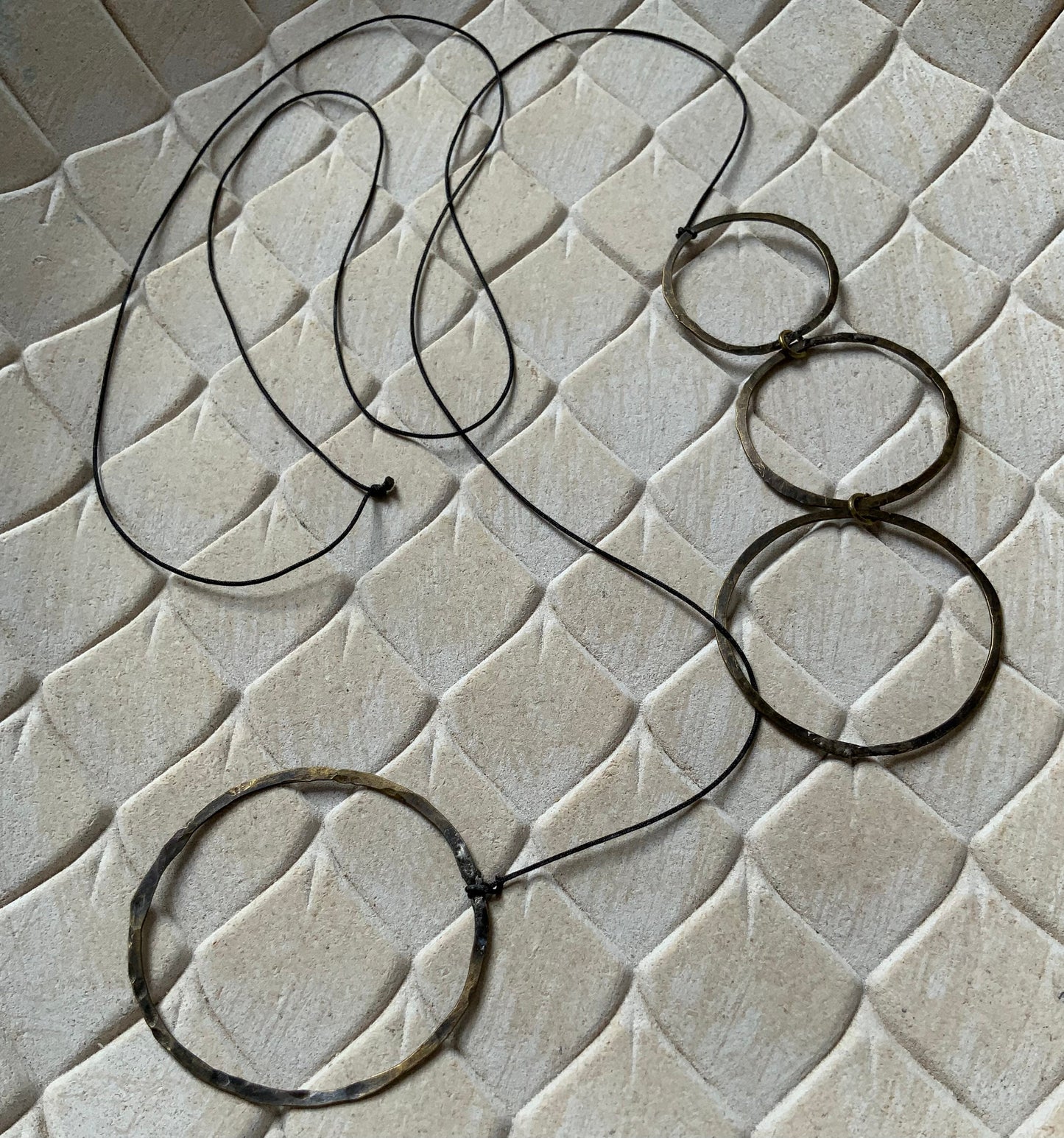 A brass necklace with cascading open circular accents, styled on a beige textured background to emphasize its modern and artistic aesthetic