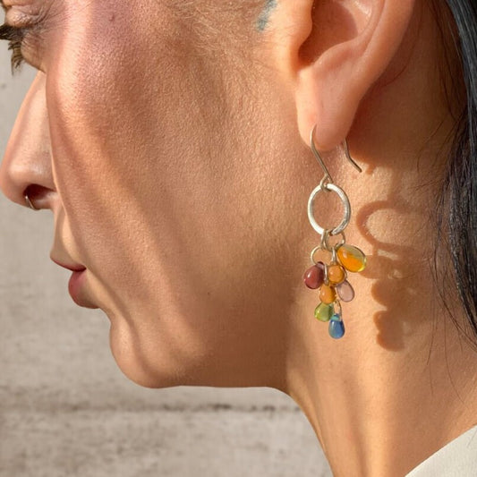 A close-up of a model wearing silver hook earrings adorned with multicolor glass teardrop pendants, styled in natural sunlight for an artistic and vibrant presentation.