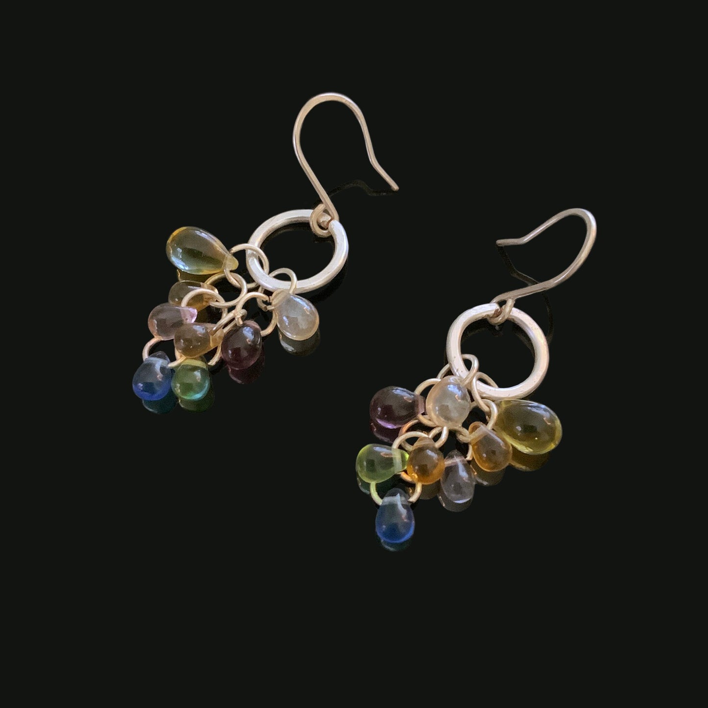 A pair of silver hook earrings featuring a cluster of multicolor glass teardrop pendants in vibrant hues, displayed on a black background to emphasize their bold and elegant design.
