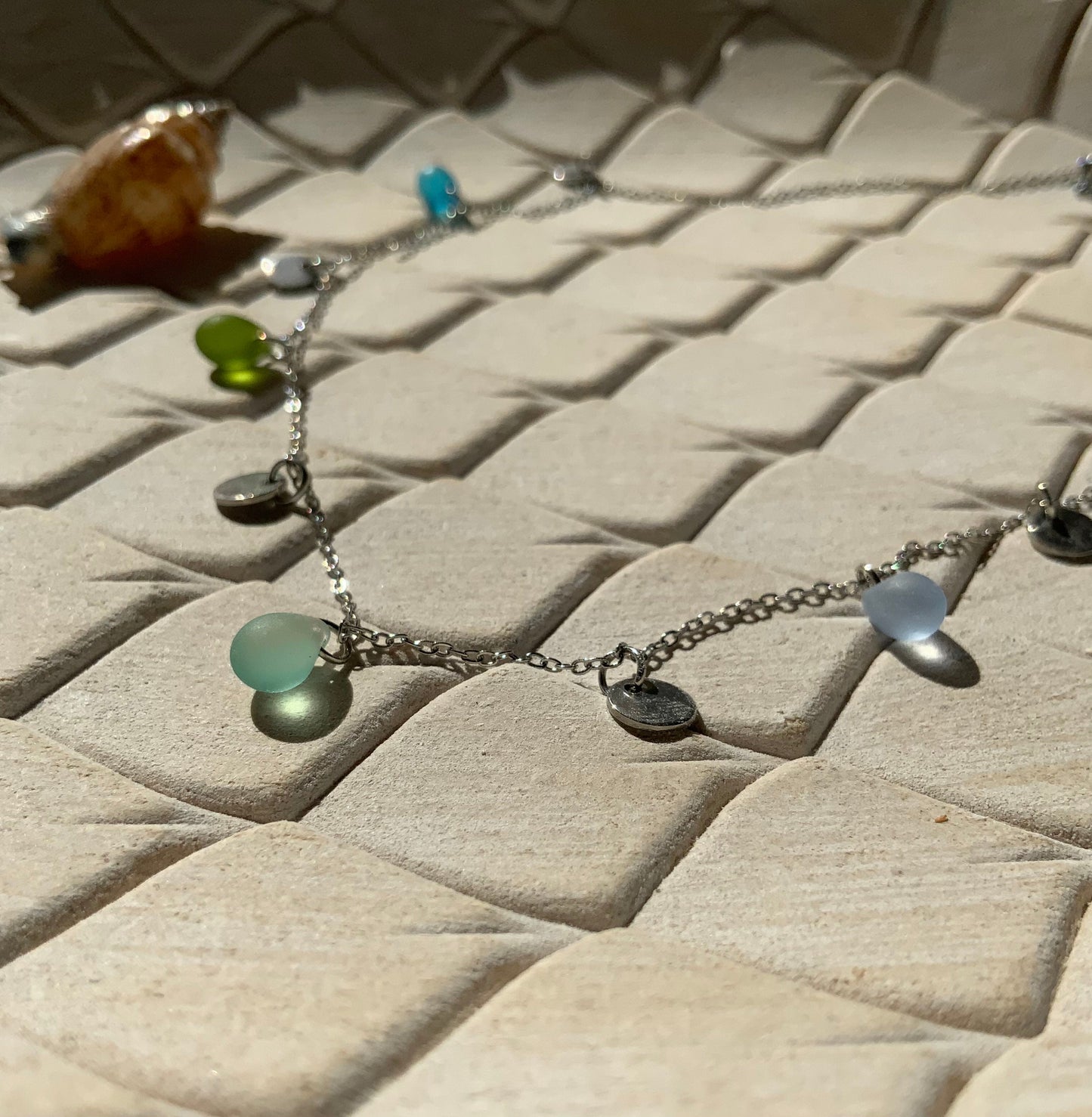 Close-up of a delicate boho-chic silver necklace with pastel sea glass beads and tiny silver coin charms, styled on white stone tiles, handmade by Jewelry by Meow