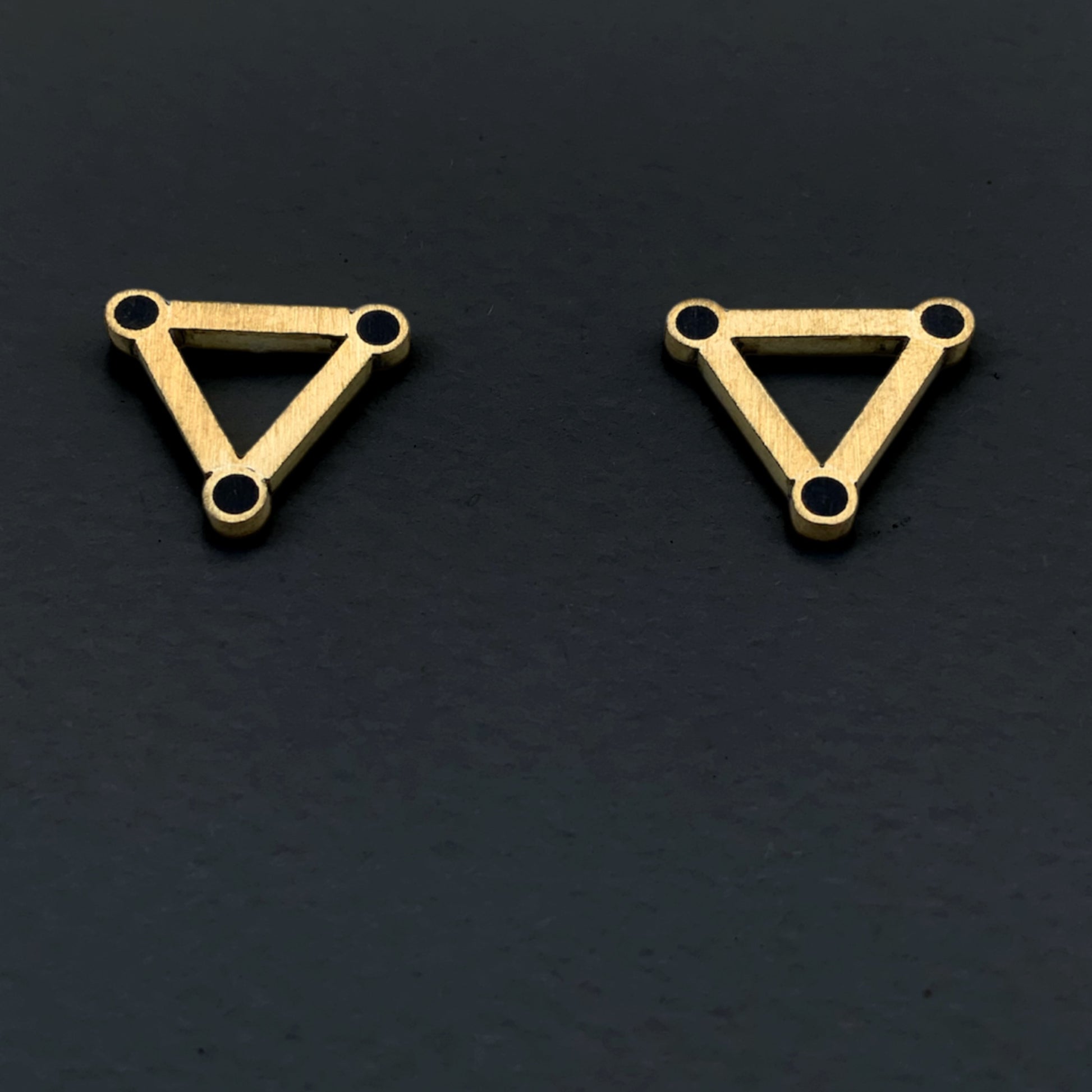 Modern brass triangle earrings with black circular details at the corners, styled on a dark background for a bold contrast.