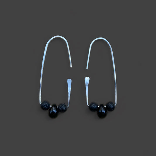 Silver handcrafted hoop earring with a smooth black glass and two lava stone beads, accented with a minimalist design. Displayed on a dark gray background for a sleek and modern look.