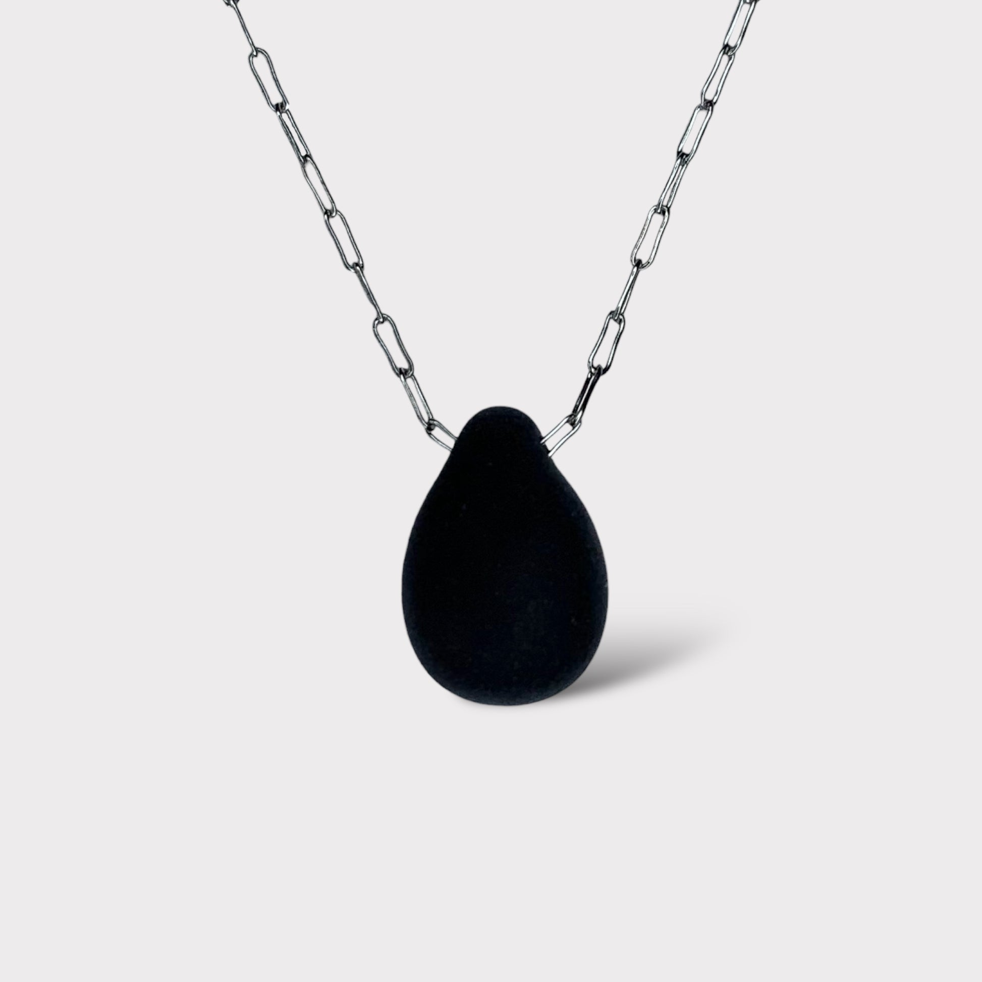 A sleek black matte teardrop-shaped glass pendant, elegantly hanging from a stainless steel chain, styled on a white background for a bold and modern look.