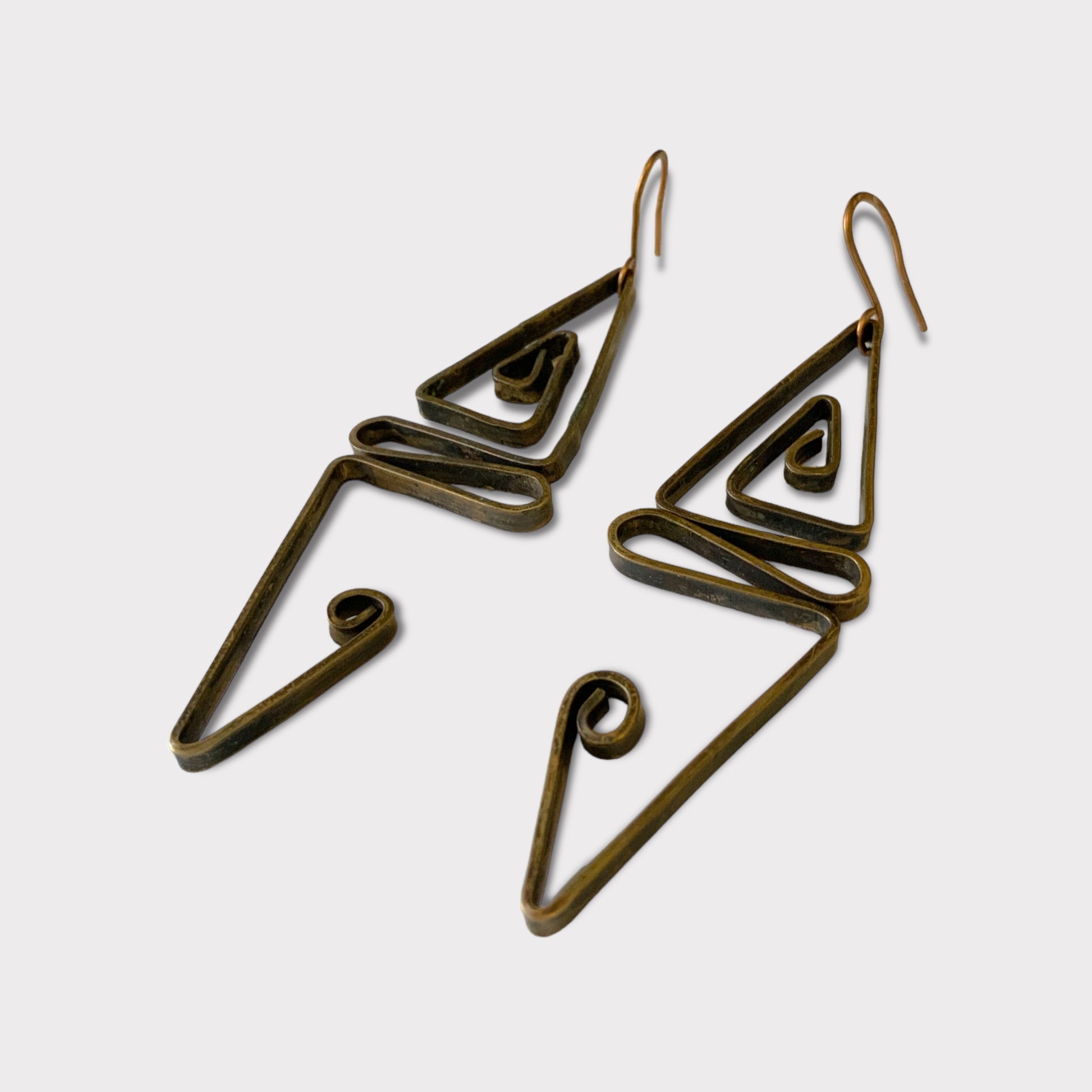 Handcrafted brass earrings with abstract geometric shapes, including triangular and spiral elements, displayed on a white background to highlight their artistic and bold design.