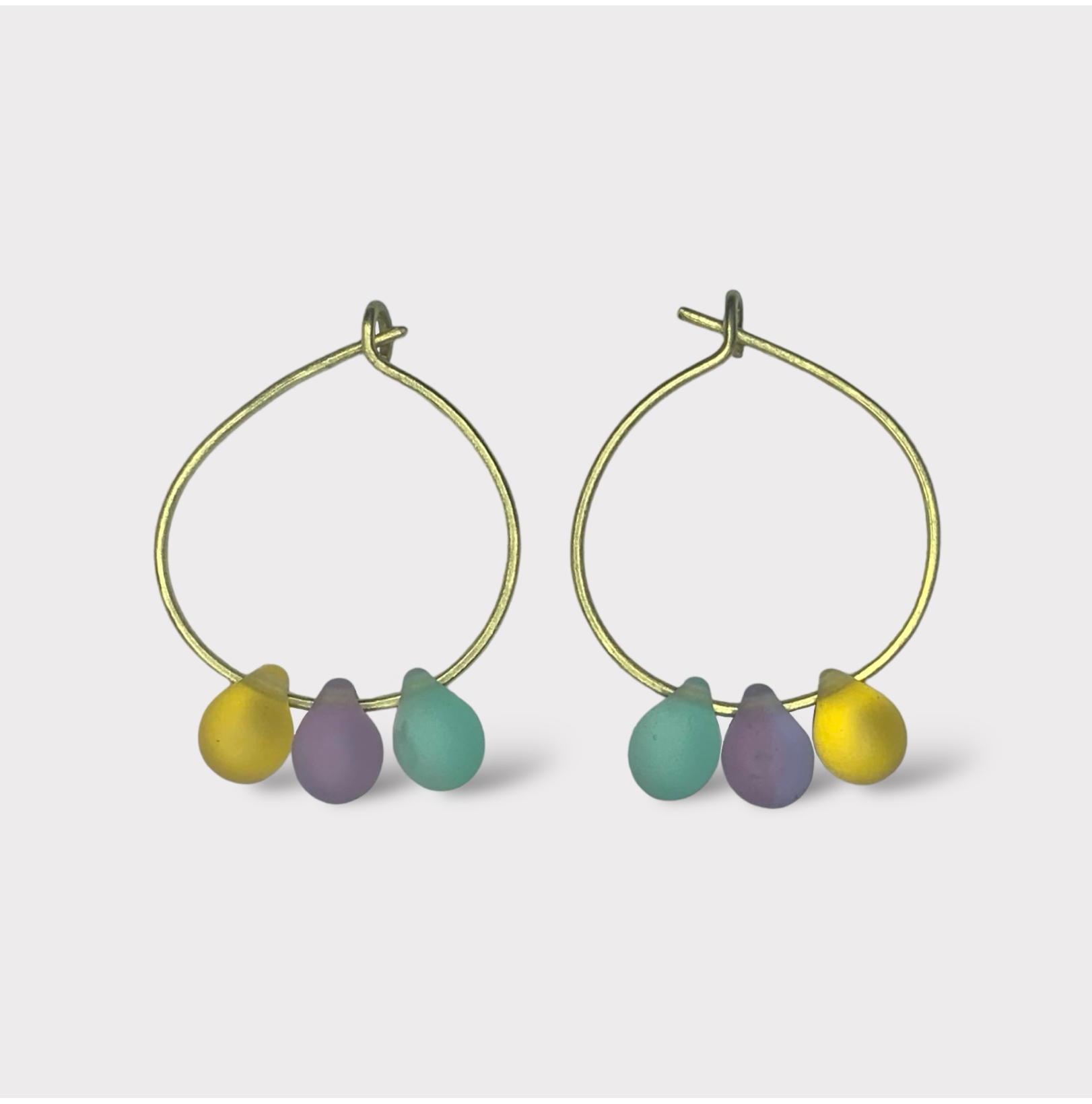 Playful gold hoop earrings featuring seaglass pendants in pastel pink, baby blue, and sunny yellow. A sweet and dreamy design reminiscent of cotton candy clouds.