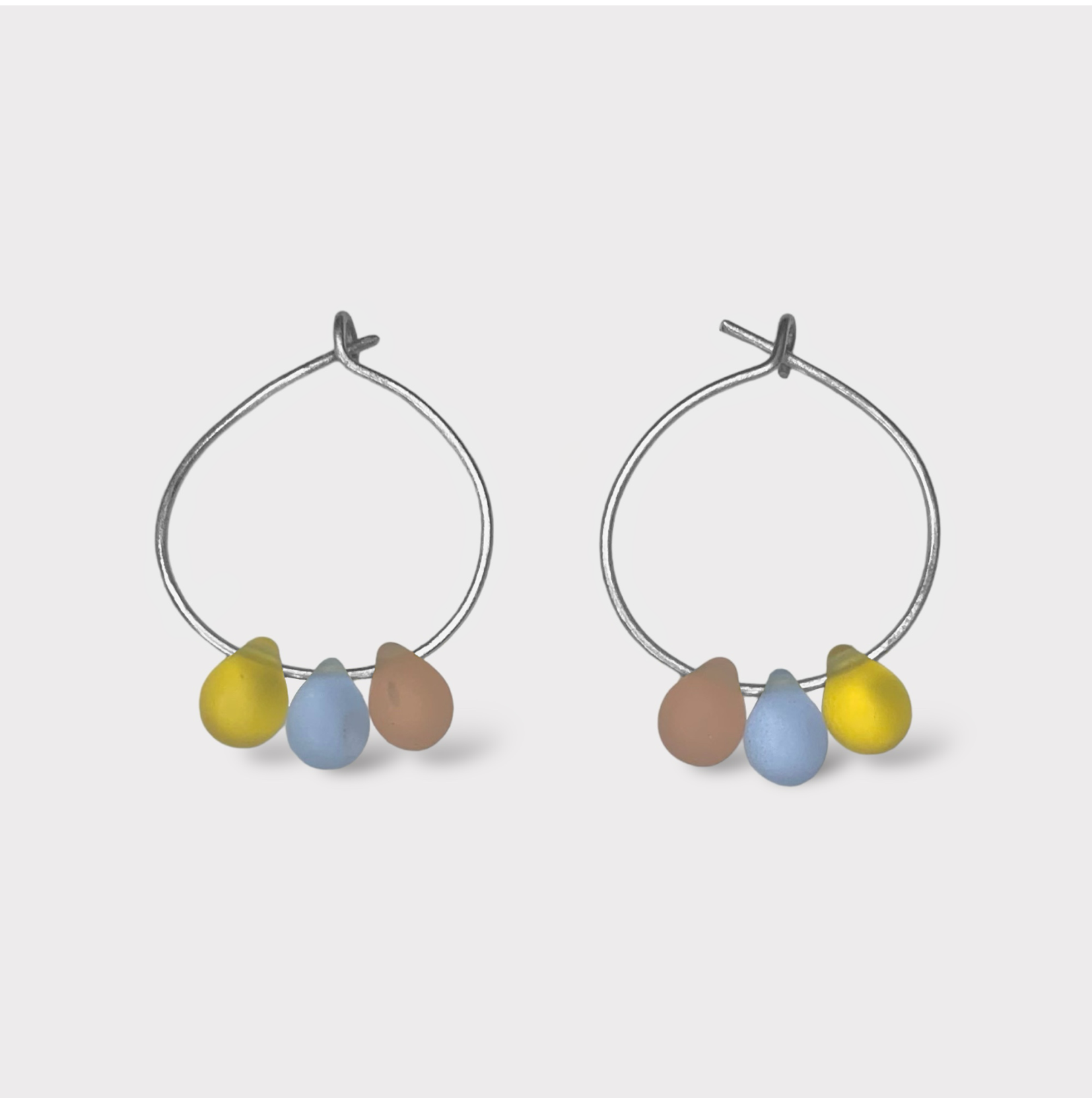 Playful silver hoop earrings featuring seaglass pendants in pastel pink, baby blue, and sunny yellow. A sweet and dreamy design reminiscent of cotton candy clouds.