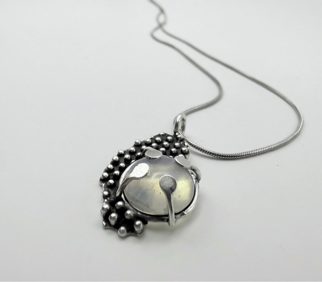 Close-up angled shot of a Dewdrop Moonstone Necklace in sterling silver with a luminous domed moonstone and droplet-textured setting on a silver snake chain