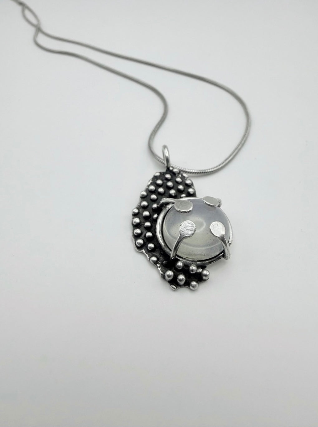Top view of the Dewdrop Halo Necklace in sterling silver with a luminous moonstone cabochon and droplet-textured setting on a silver snake chain